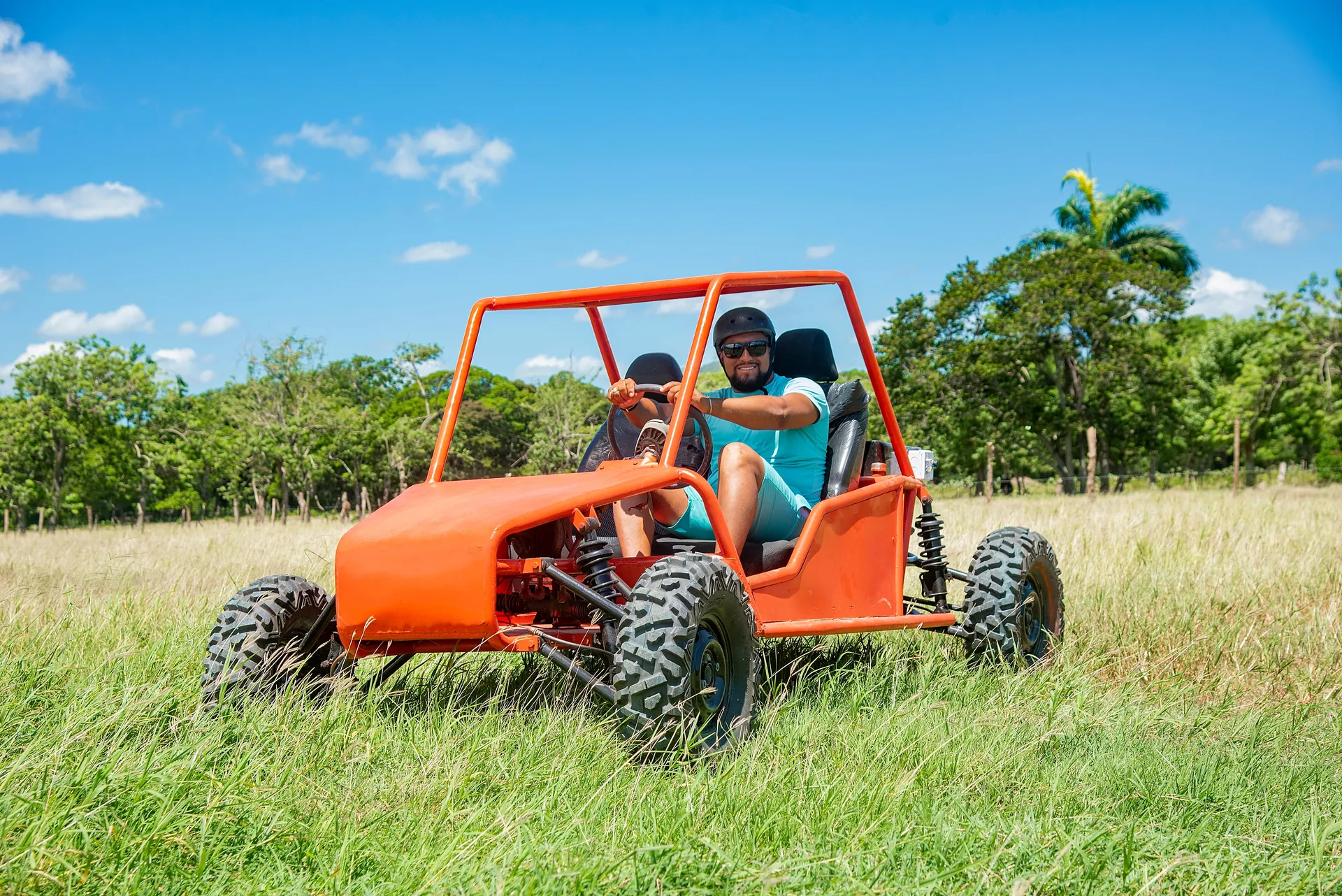 A man in sunglasses enjoys a ride in an orange dune buggy on a sunny day.
