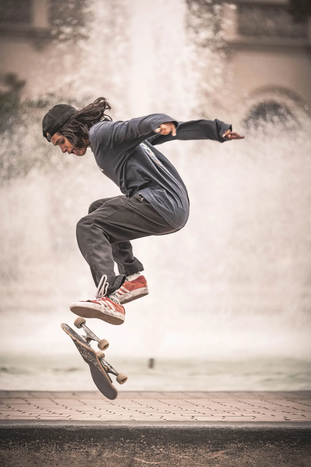 Energetic skateboarder performing a mid-air trick in front of a fountain.