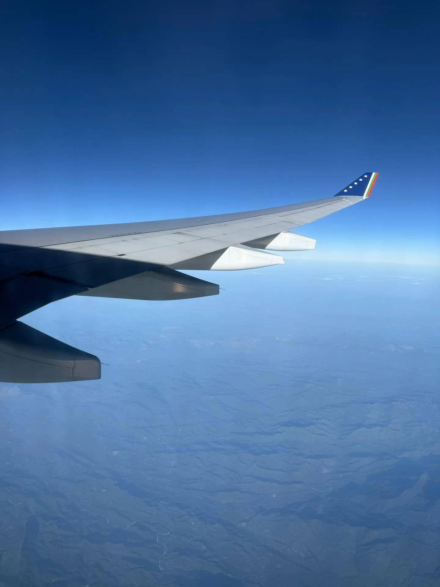 A tranquil view from an airplane wing over a vast blue horizon, showcasing the beauty above the clouds.
