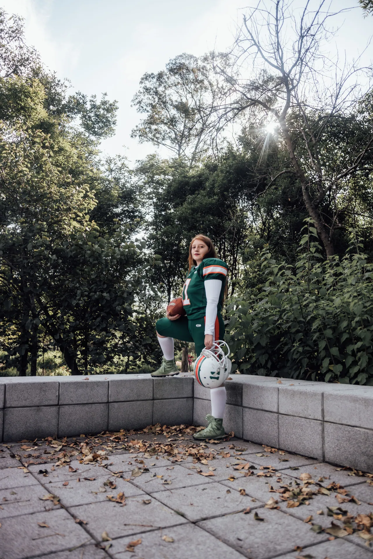 Confident female athlete in football gear poses outdoors in a lush park setting in Mexico City.