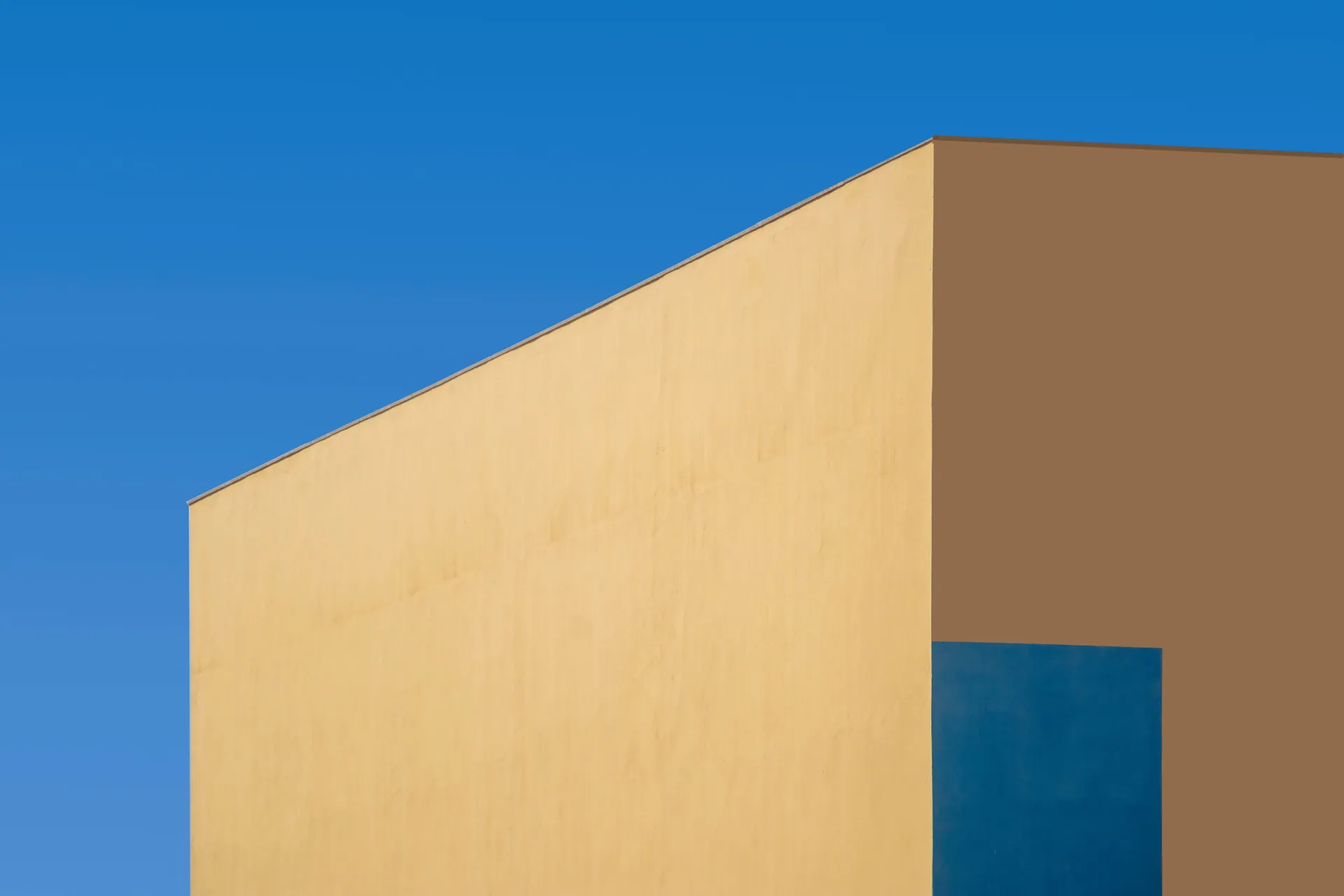 Minimalist architectural shot featuring a modern yellow and blue building under a clear blue sky.