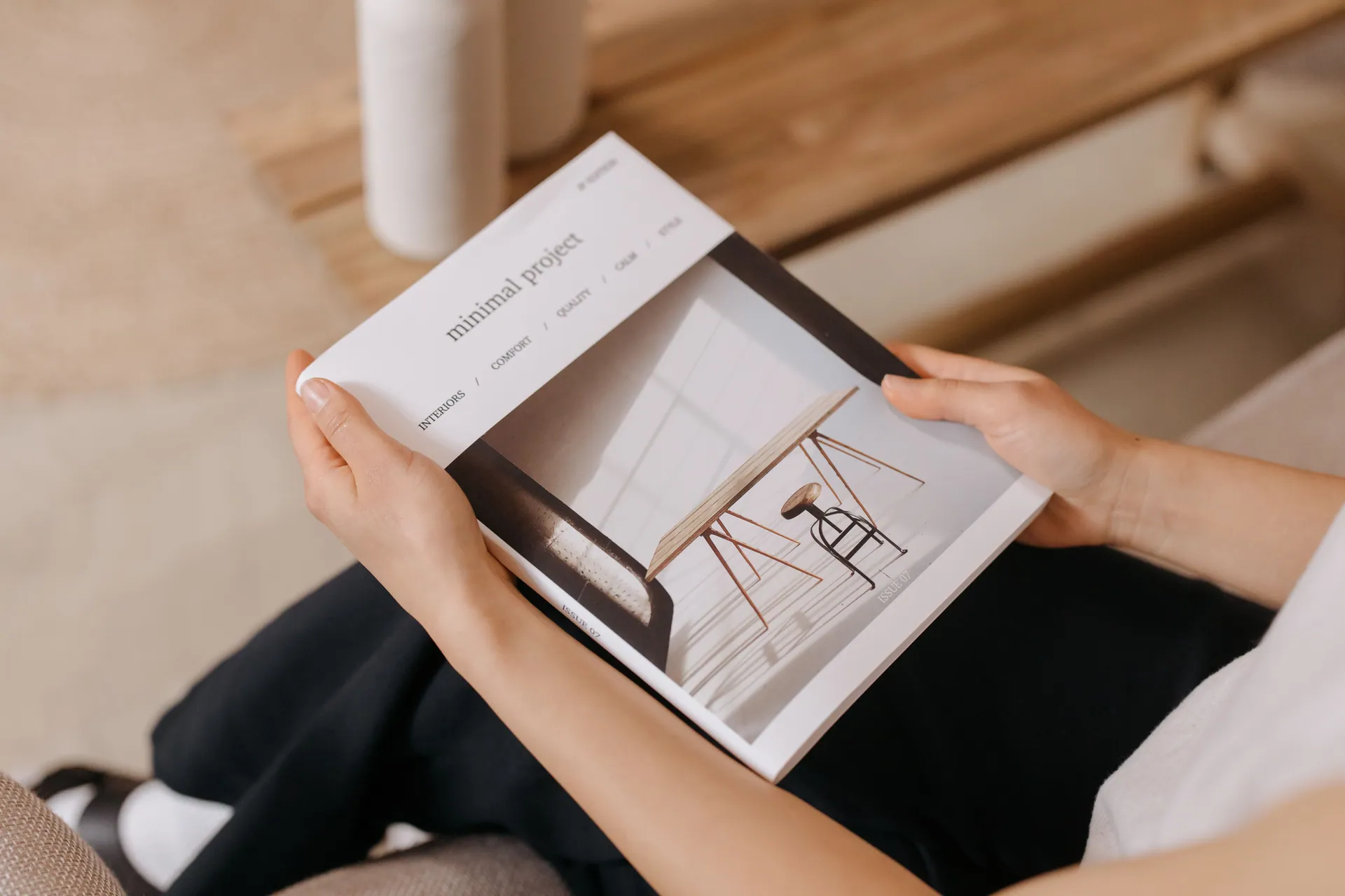 Person relaxing indoors while reading a minimalist design magazine, showcasing modern aesthetics.