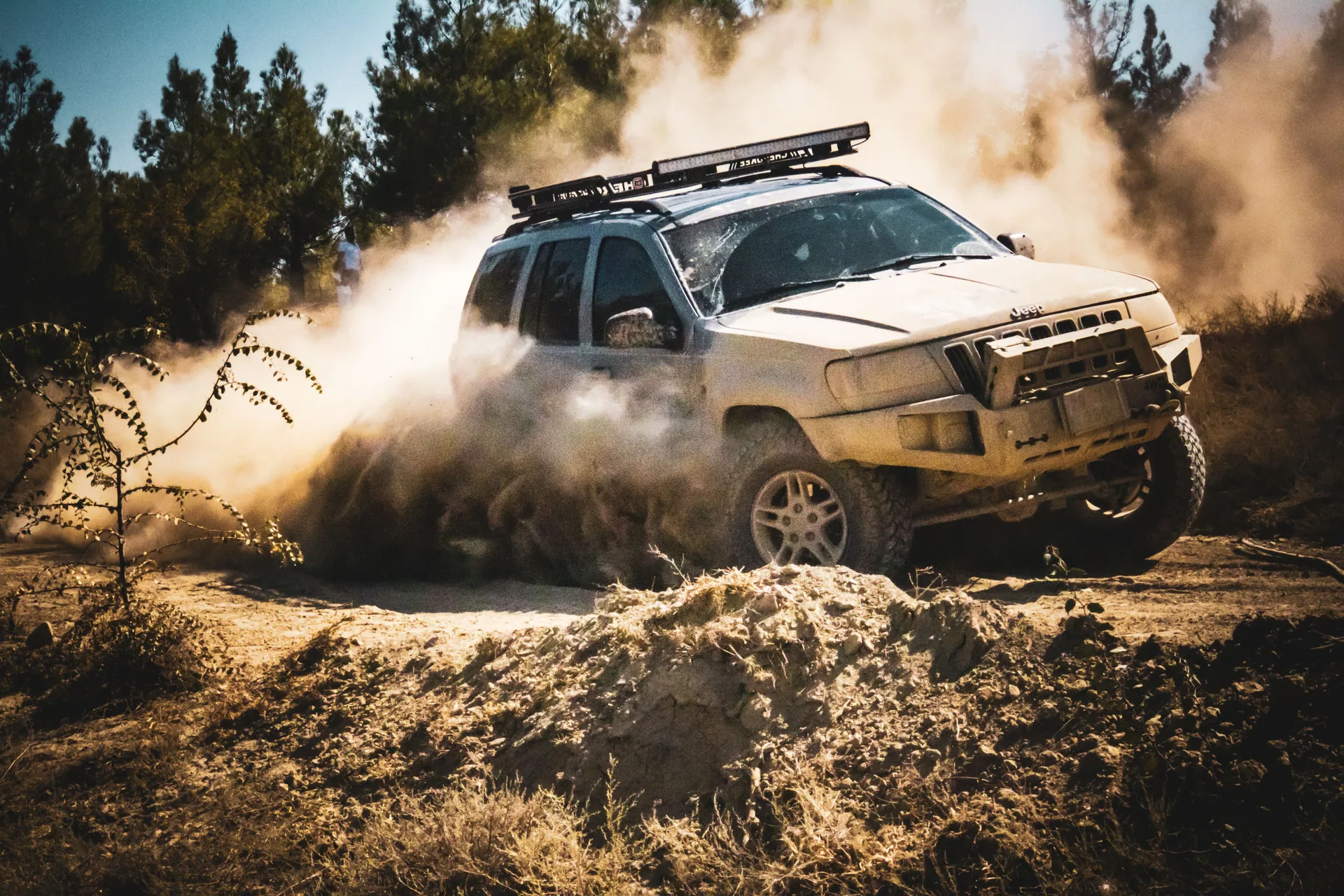 An SUV speeds through a dusty dirt road in a forest setting, showcasing off-road capabilities.