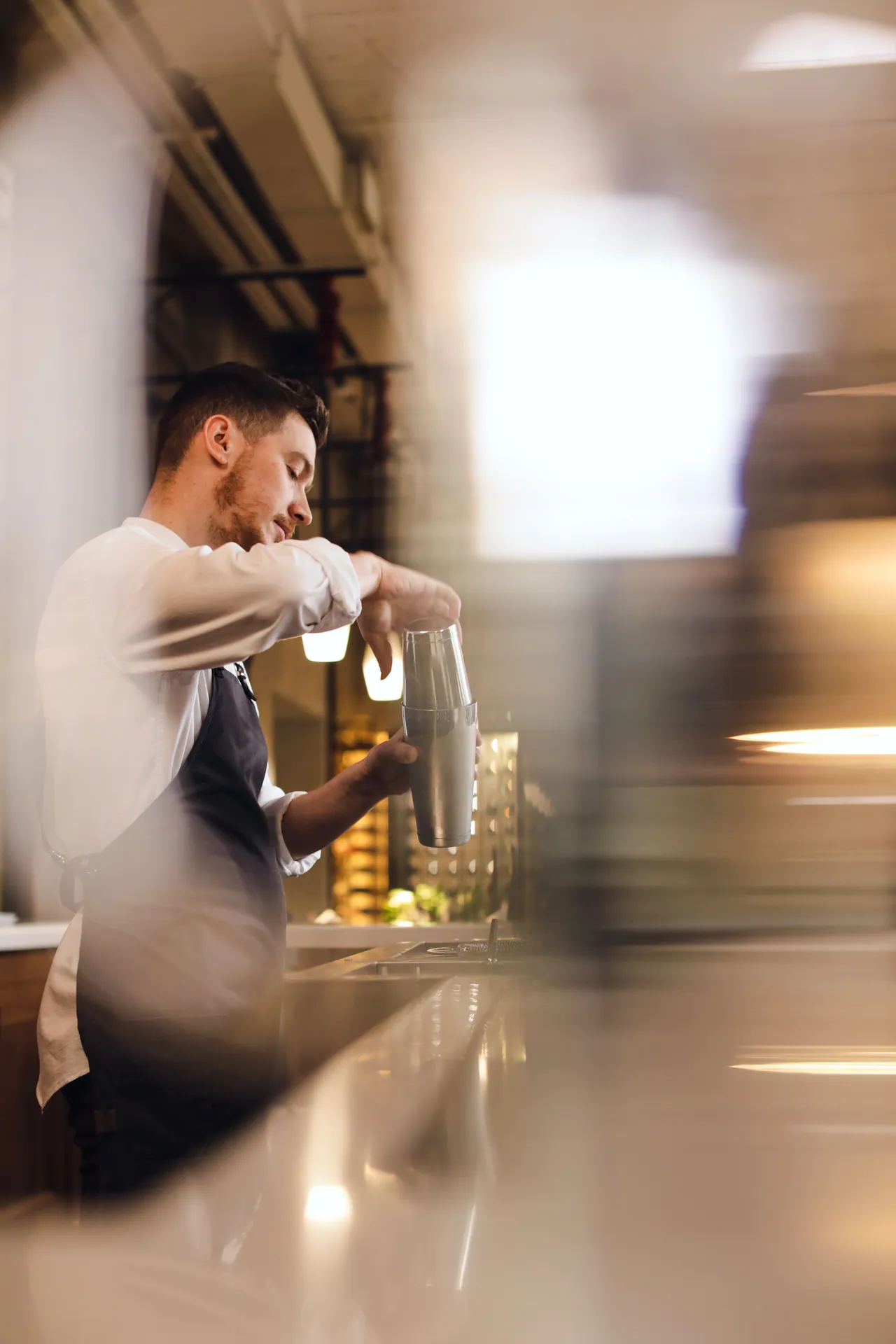 Side view of a bartender skillfully mixing a drink with a shaker indoors.