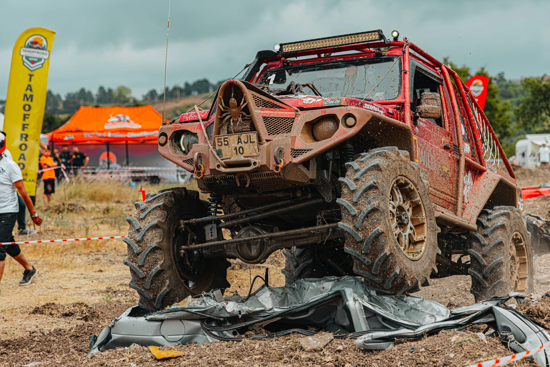Red off-road vehicle tackling challenging outdoor race through rugged, muddy terrain.