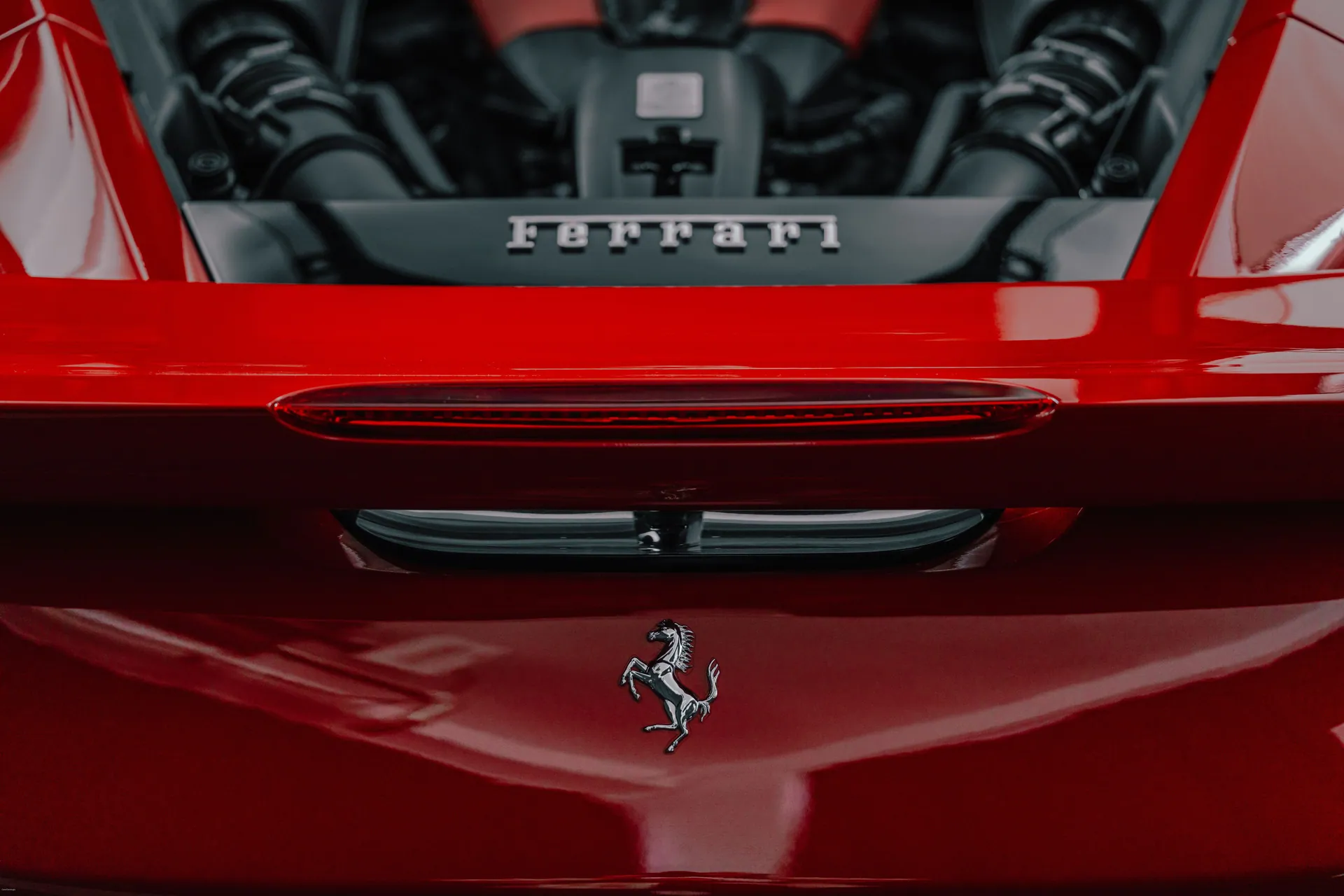 Detailed close-up of a red sports car exhibiting the emblem and engine bay, highlighting luxury and performance.
