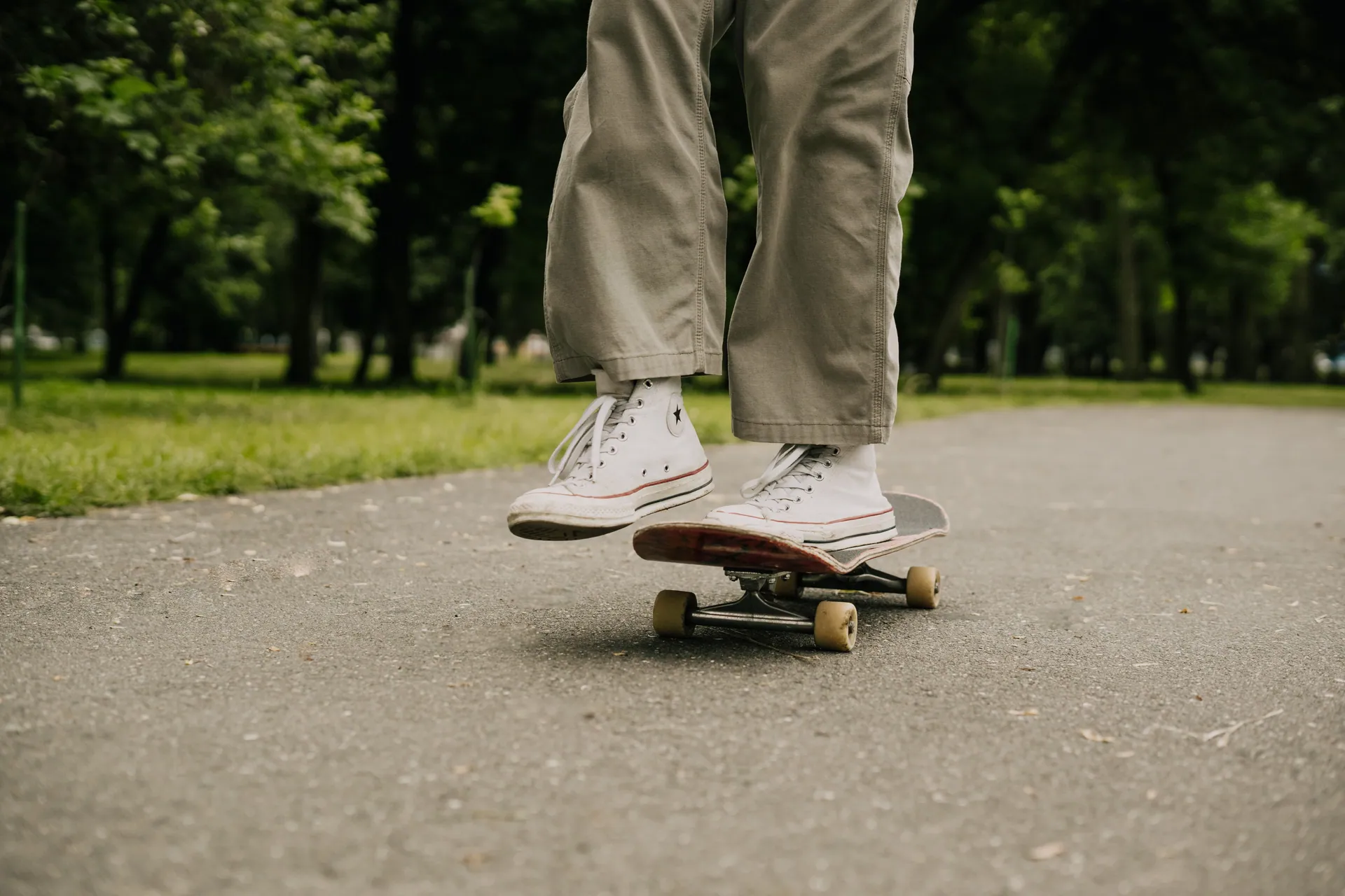 Close-up of a skateboarder's feet performing a trick in a sunny park setting.