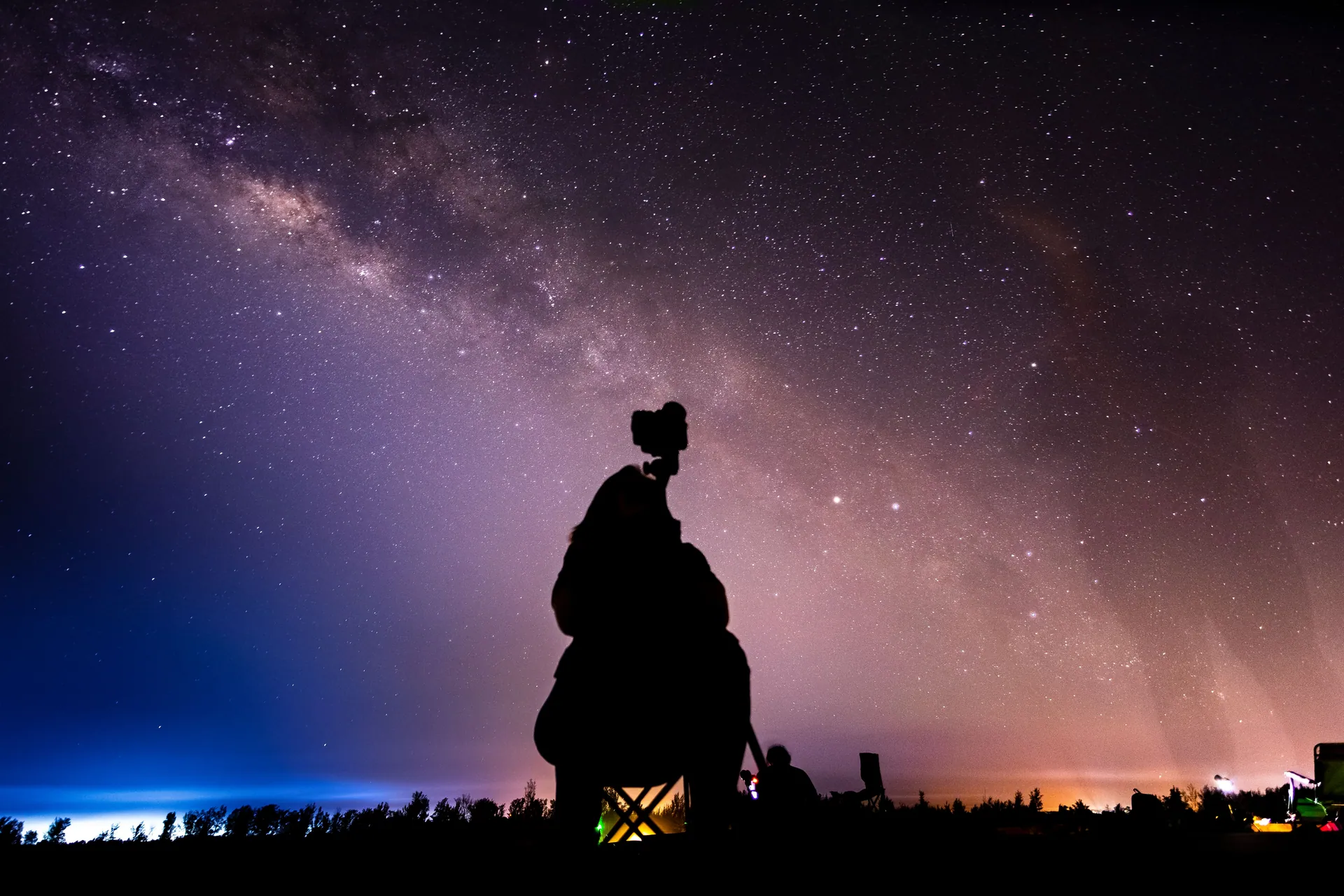 Silhouette of a stargazer with camera capturing the Milky Way under a stunning star-filled night sky.