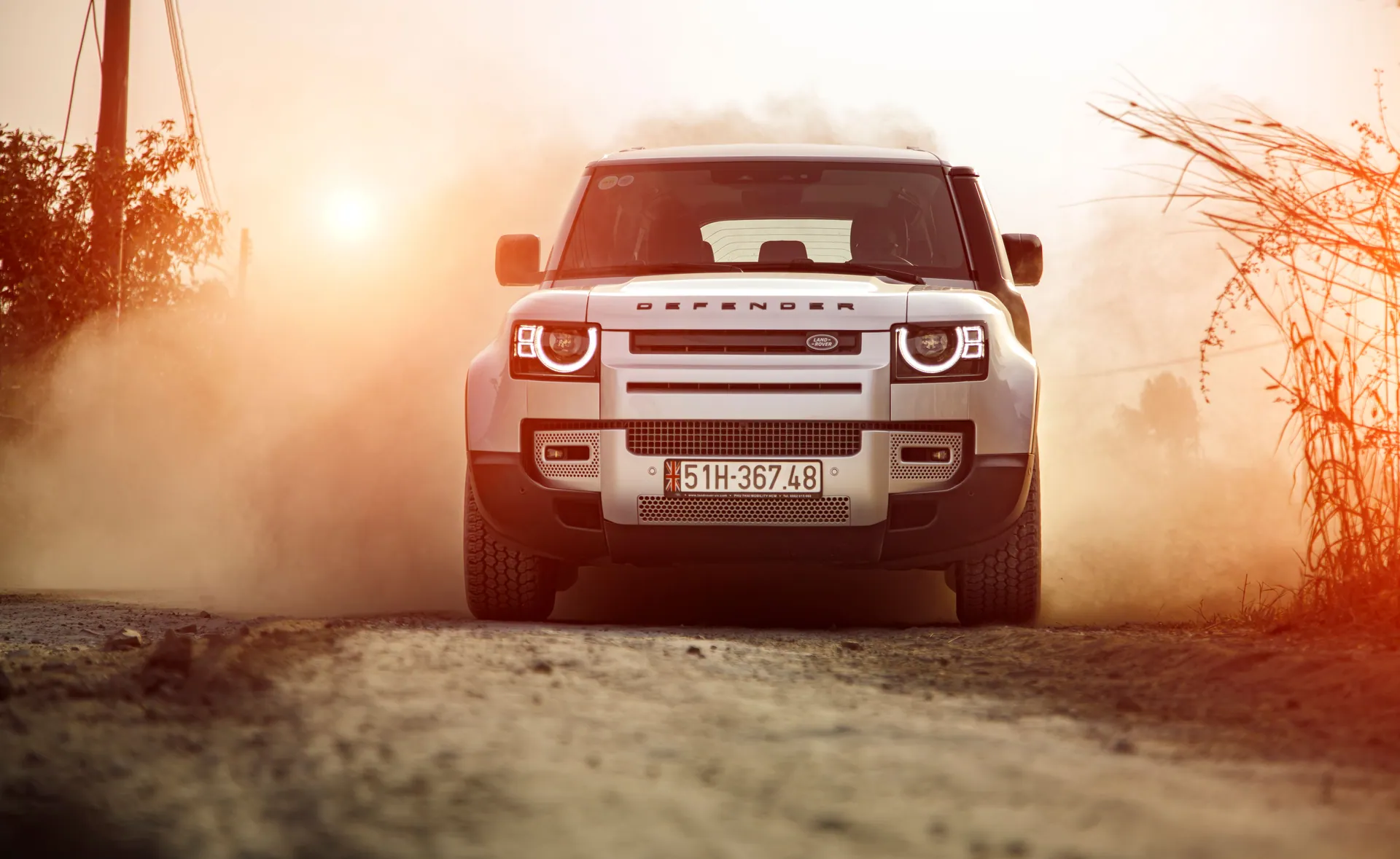 Land Rover Defender driving on a dusty road at sunset, embodying adventure and rugged capability.