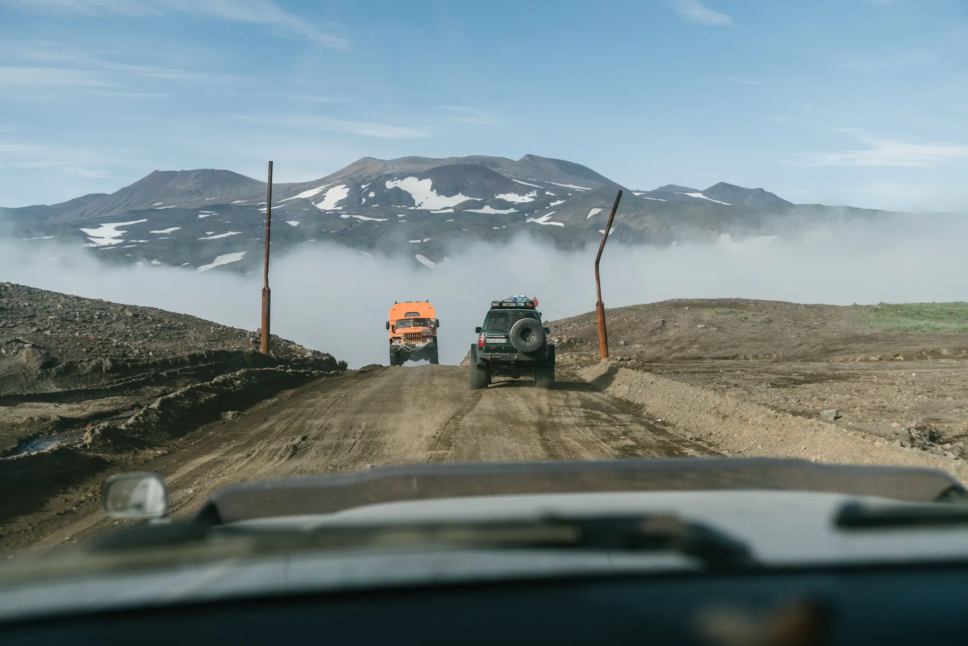 Rugged 4x4 vehicles navigating a dirt road through misty mountain landscapes.
