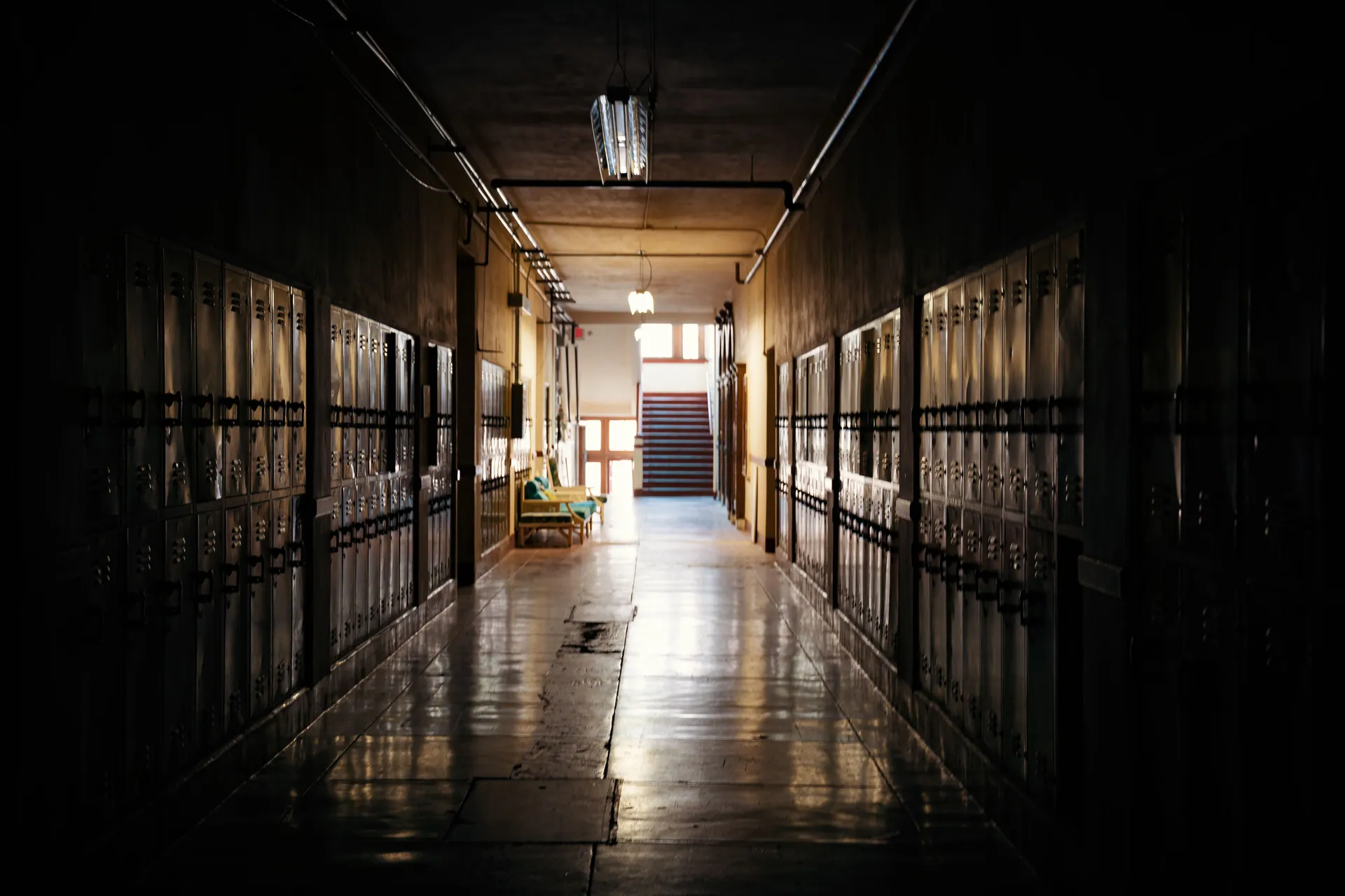 A dark and moody school hallway with lockers and a distant light source.
