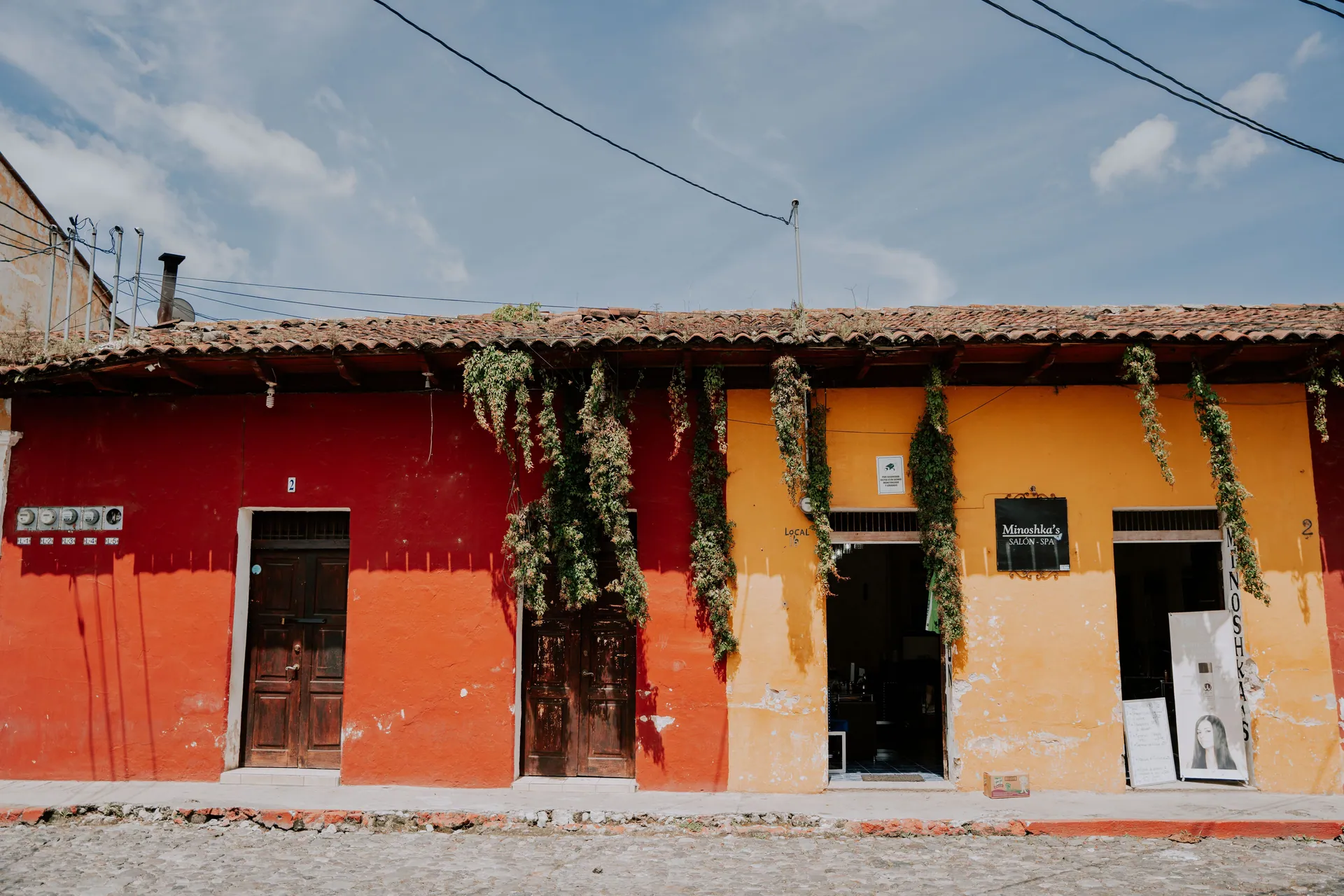 Vibrant red and yellow townhouses with hanging plants under a blue sky.