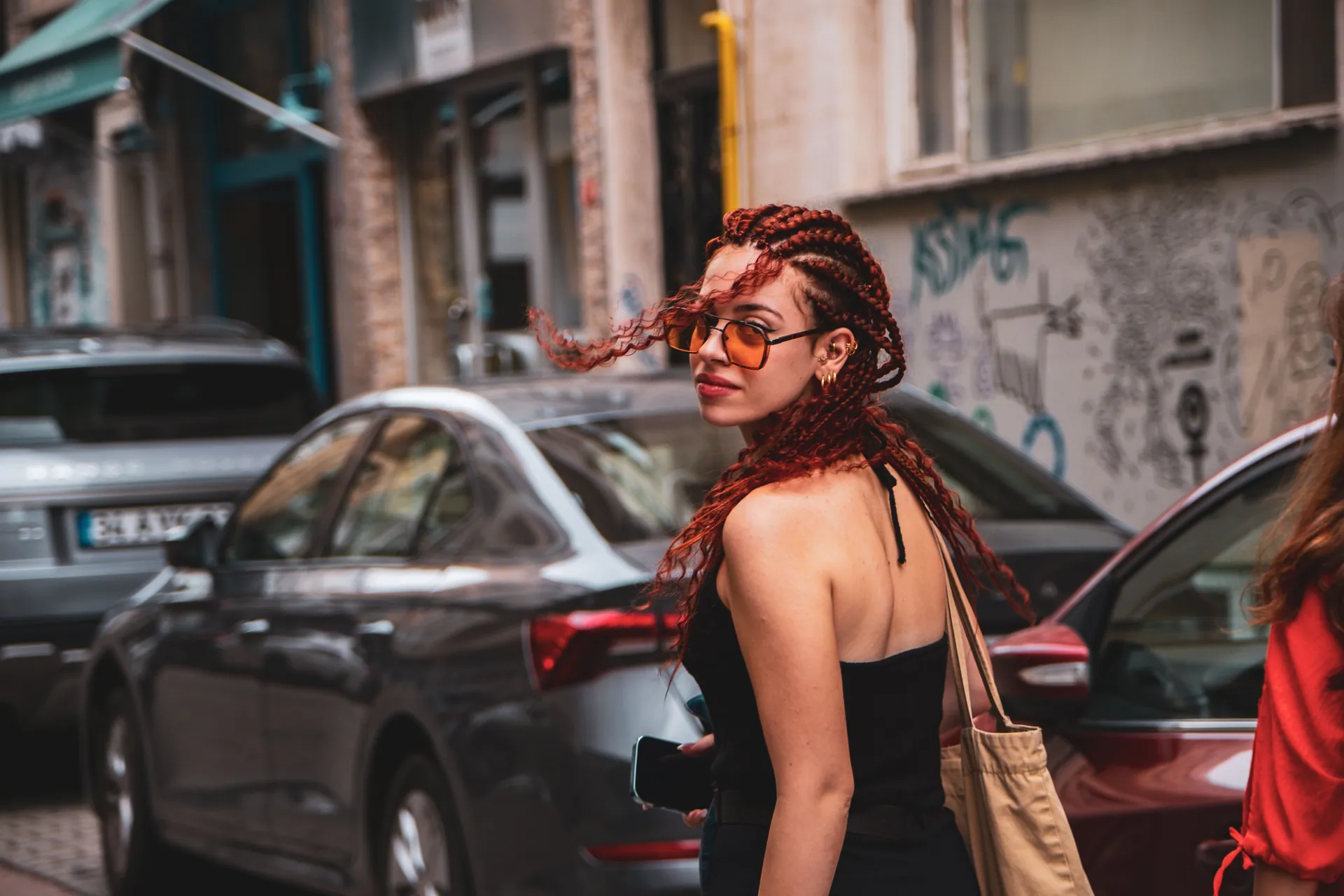Redhead woman with stylish braids and sunglasses walking on city street.