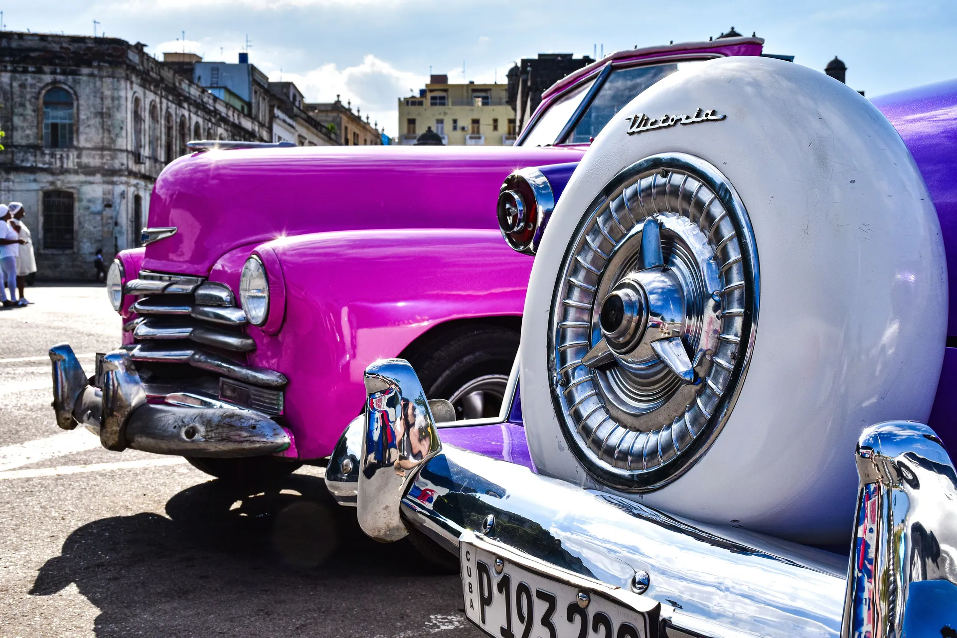 Close-up of classic pink cars in a Cuban town, showcasing vintage charm and urban culture.