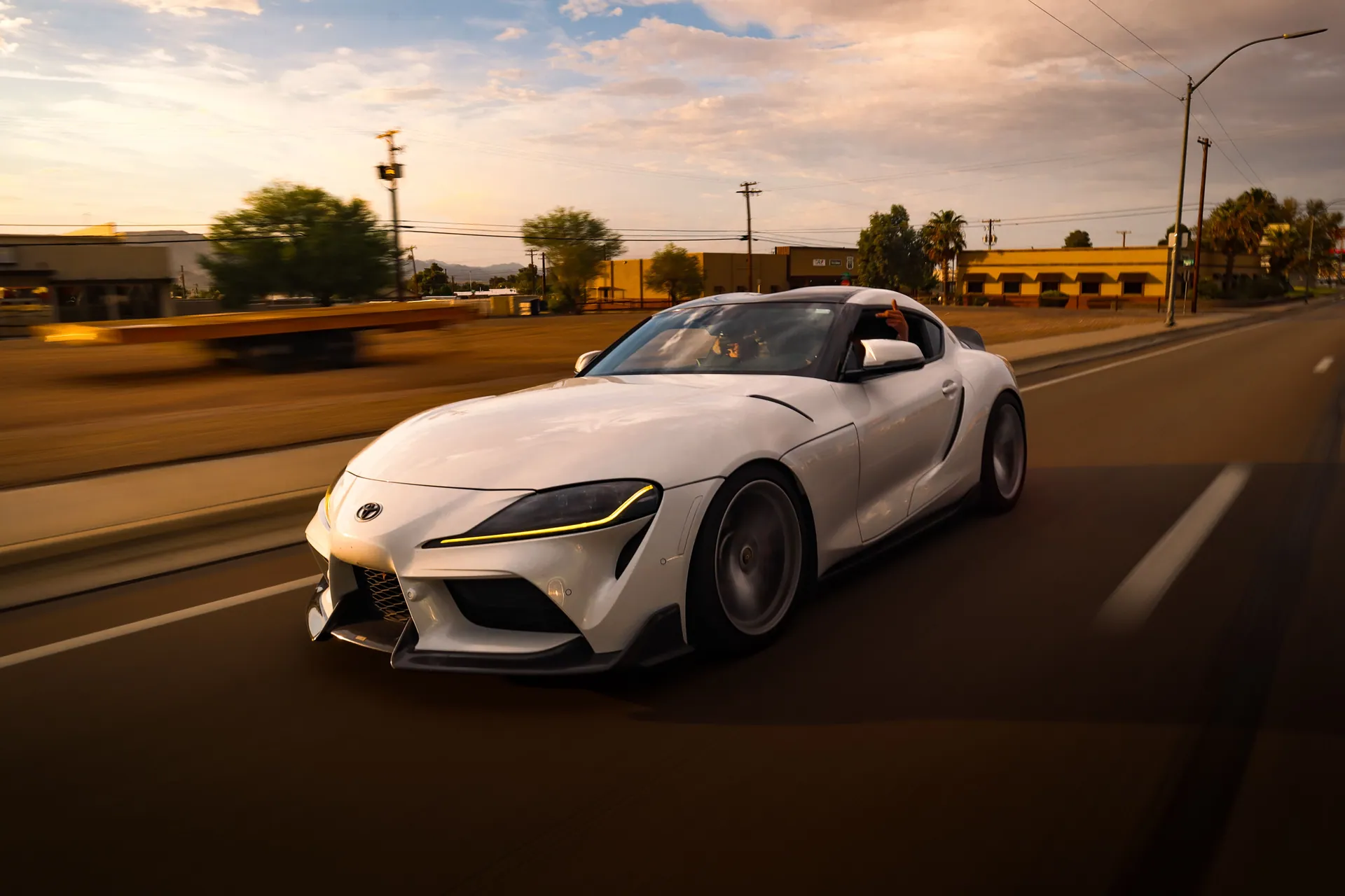 Dynamic shot of a white sports car speeding down a road at sunset.