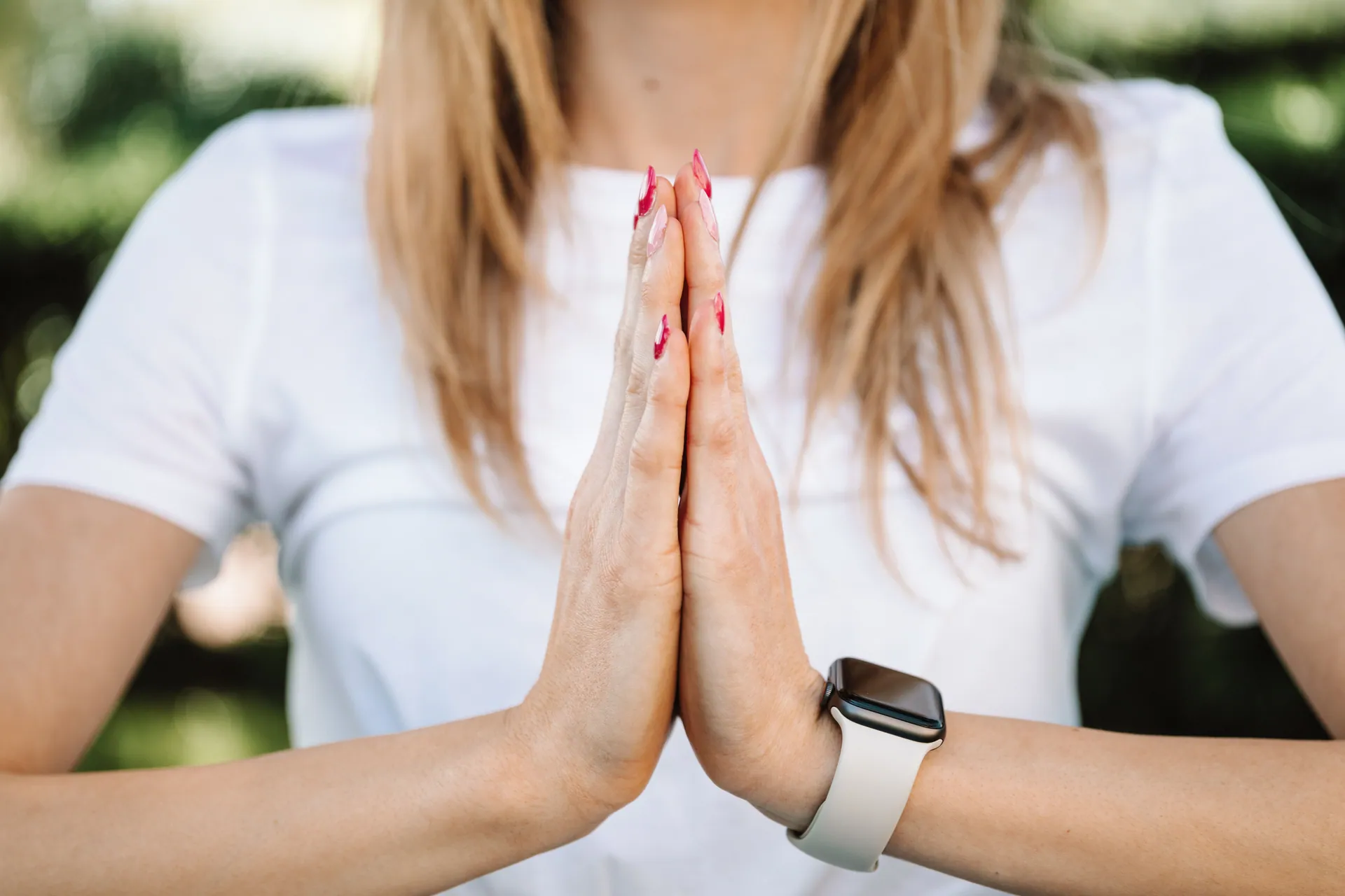 Close-up of woman in prayer pose wearing a smartwatch, symbolizing modern lifestyle and wellness.