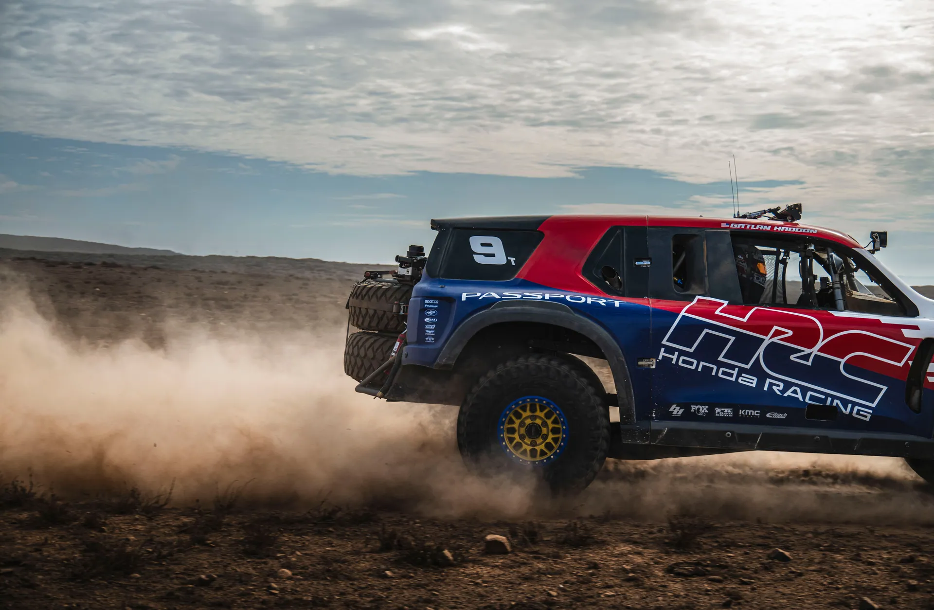A powerful off-road truck races through the dusty Baja California desert terrain.