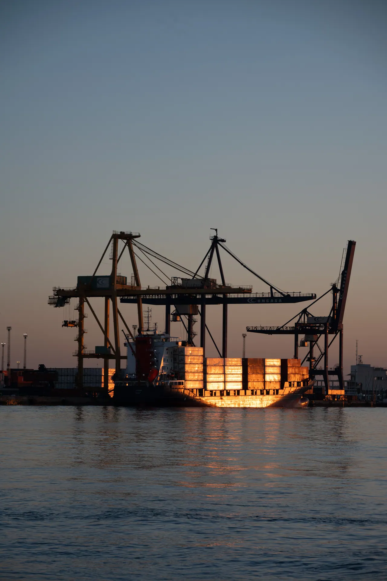 A container ship illuminated by sunset at a bustling port, showcasing maritime industry.
