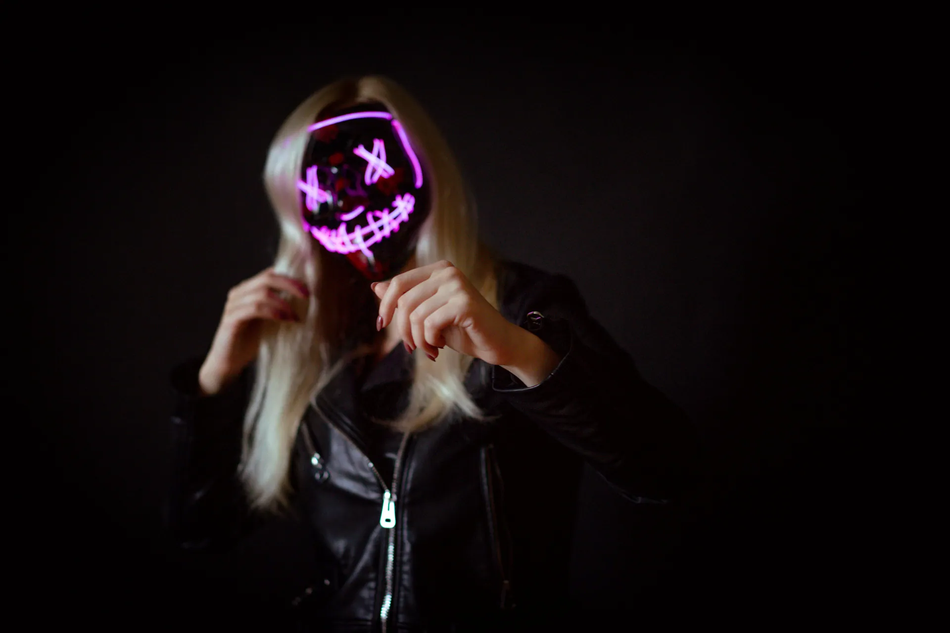A woman wearing a neon mask and leather jacket creates a spooky fashion statement against a black background.