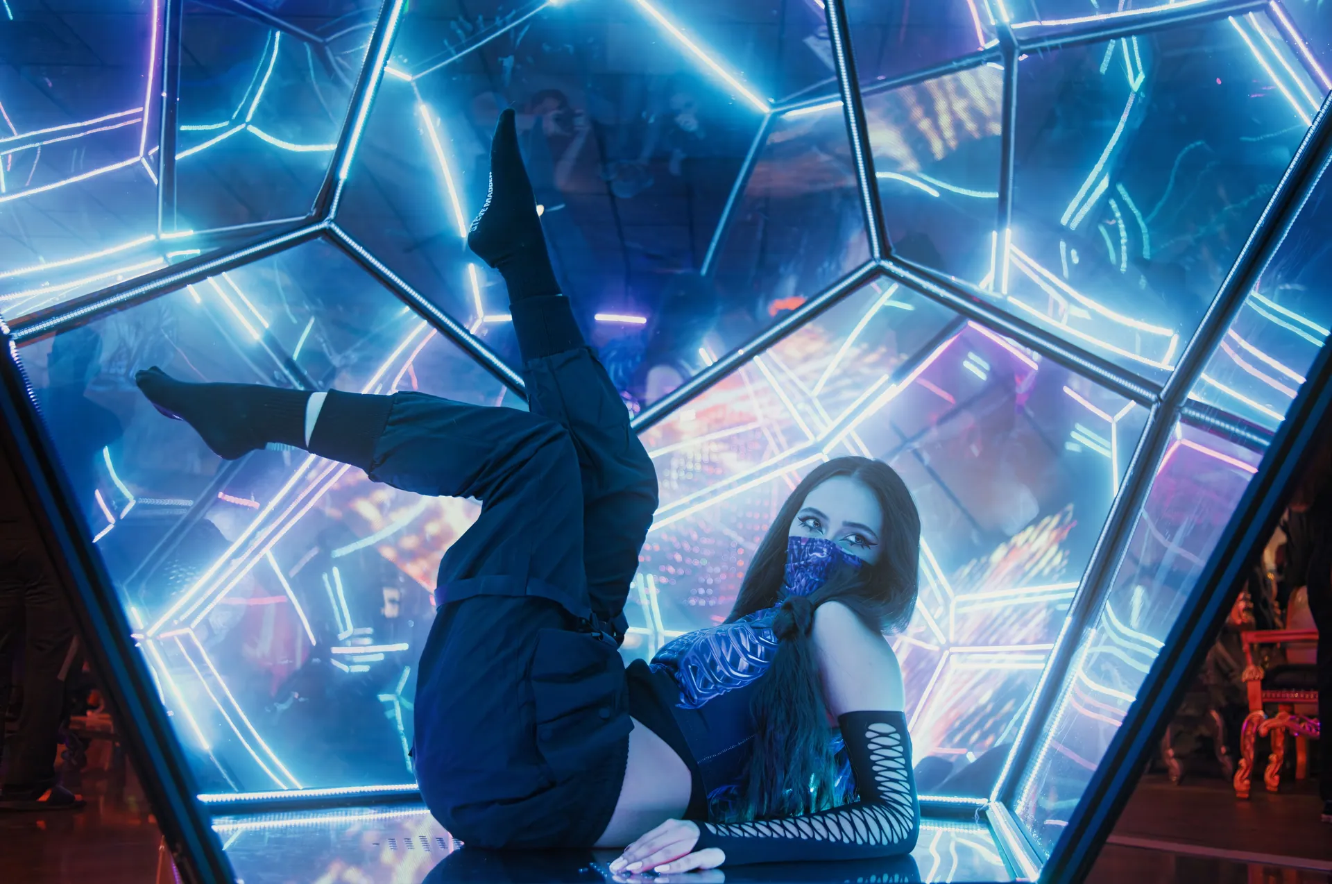 Woman in futuristic outfit poses amidst neon lights, combining artistry and technology.