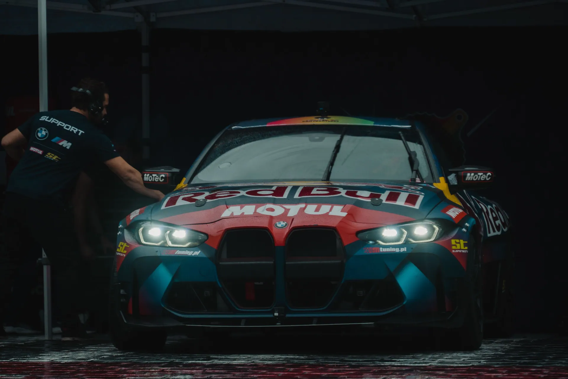 Front view of a BMW M4 race car featuring Red Bull Motul branding under dim lighting.