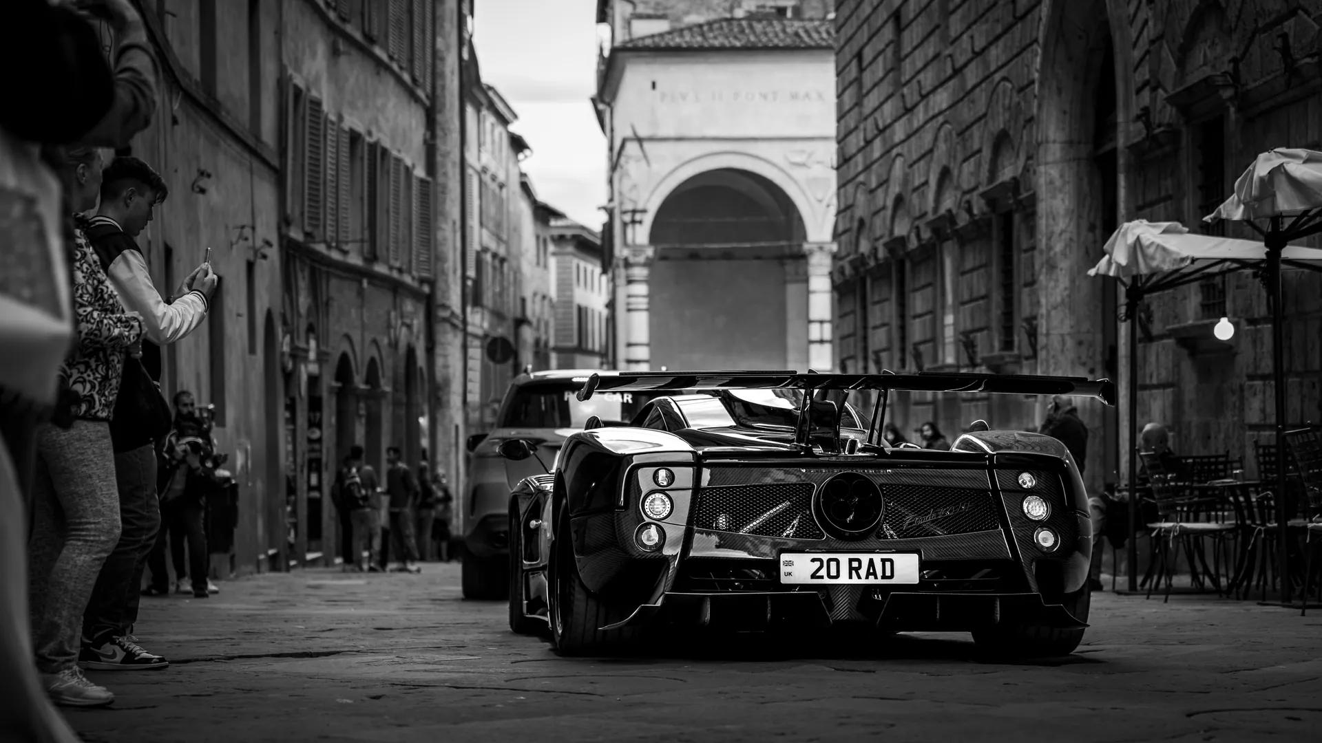 Black and white photo of a supercar driving through an historic urban street.