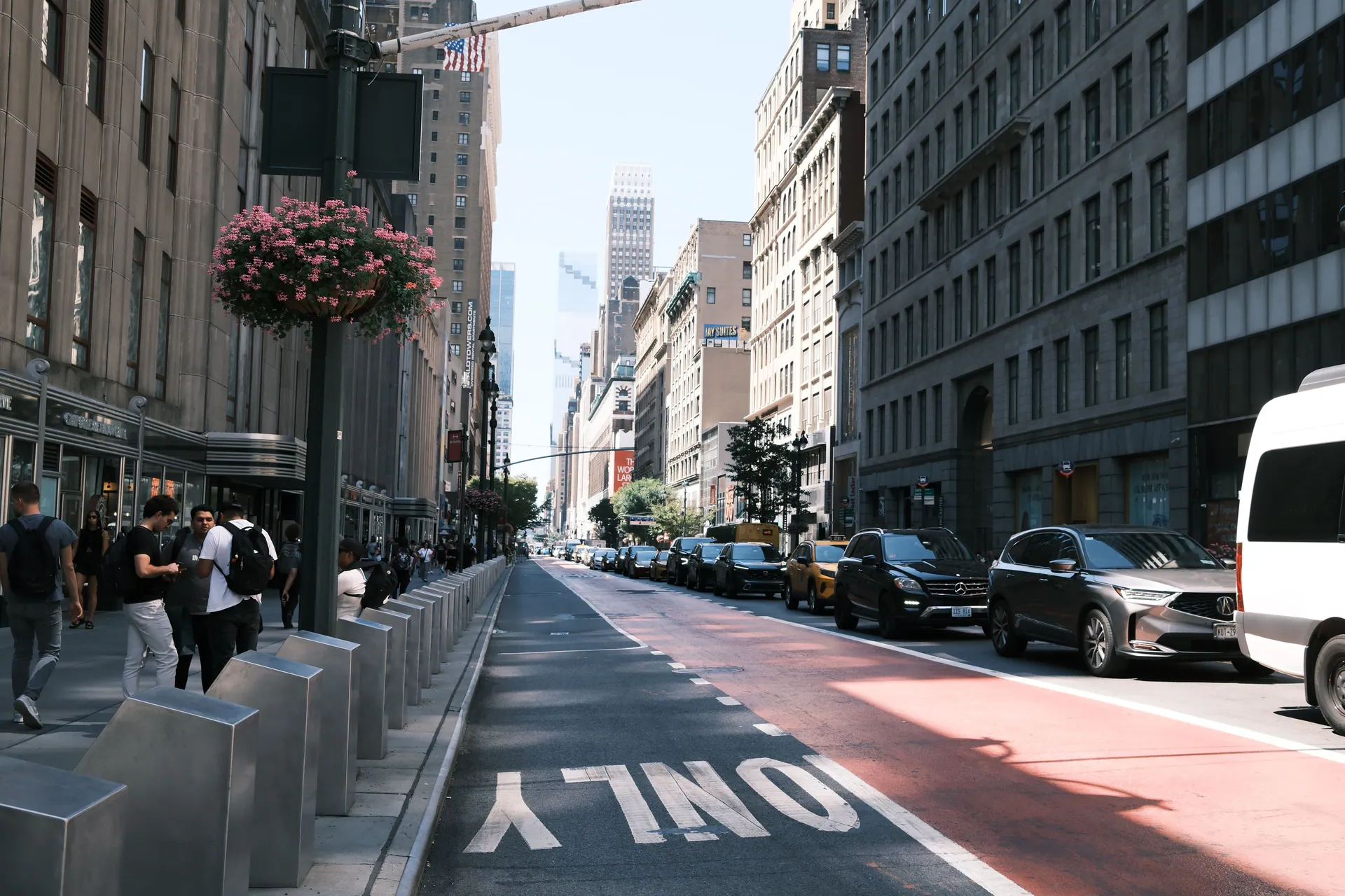A lively street in New York City with people, cars, and tall buildings under a clear sky.