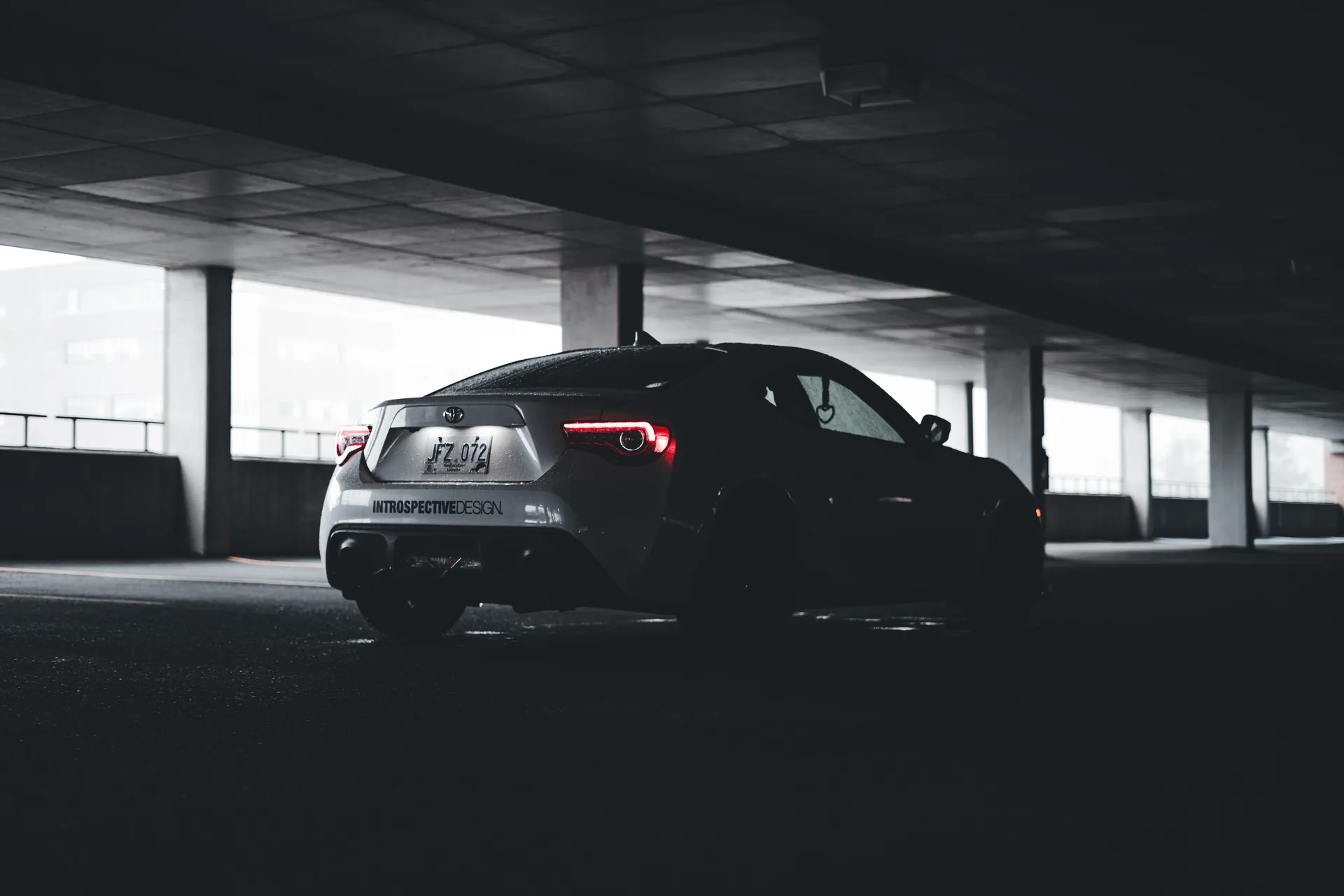 A stylish sports car with illuminated taillights parked in a dimly lit urban garage, showcasing modern design aesthetics.