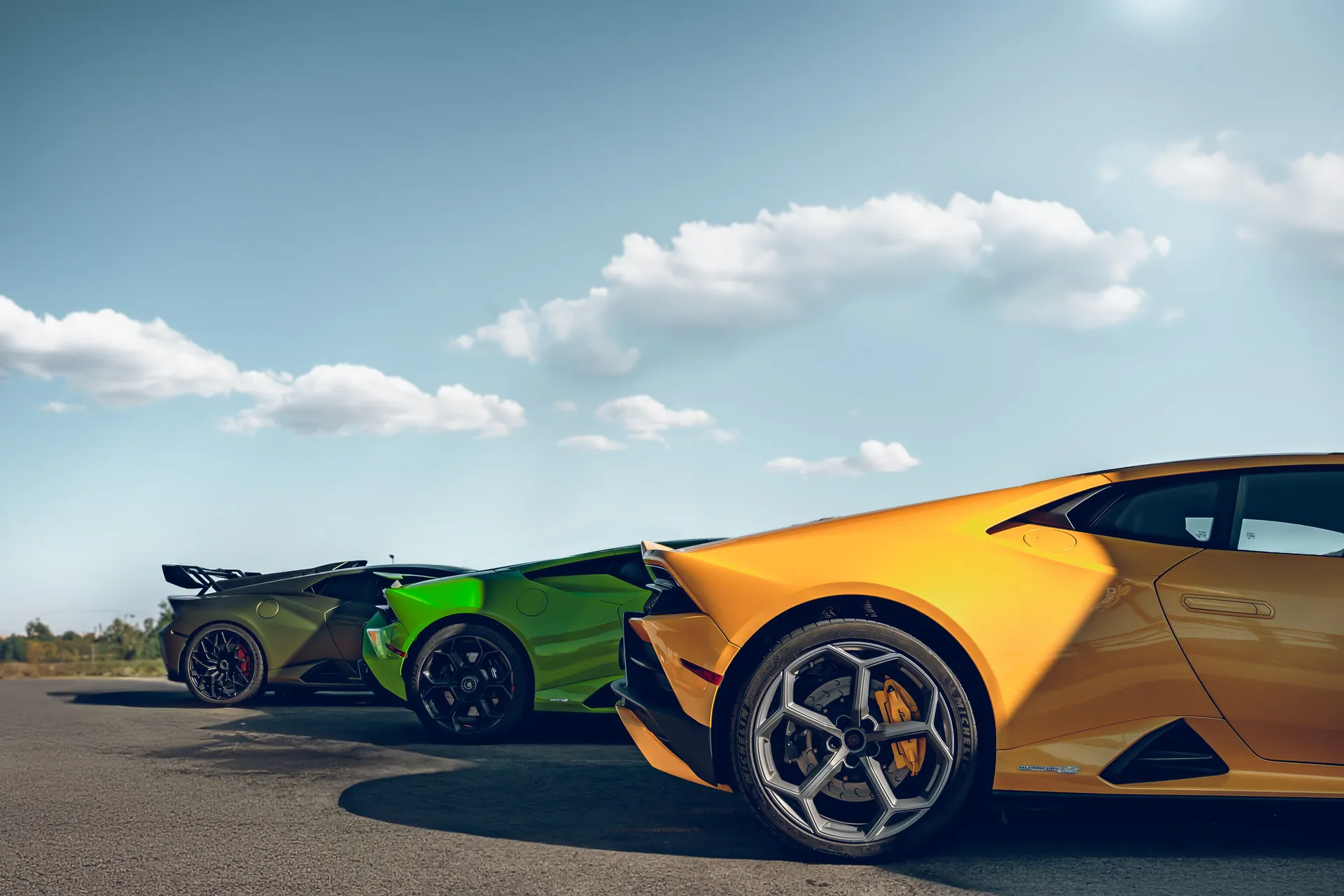 Vibrant Lamborghini Huracan supercars in different colors parked on a sunny, open road.