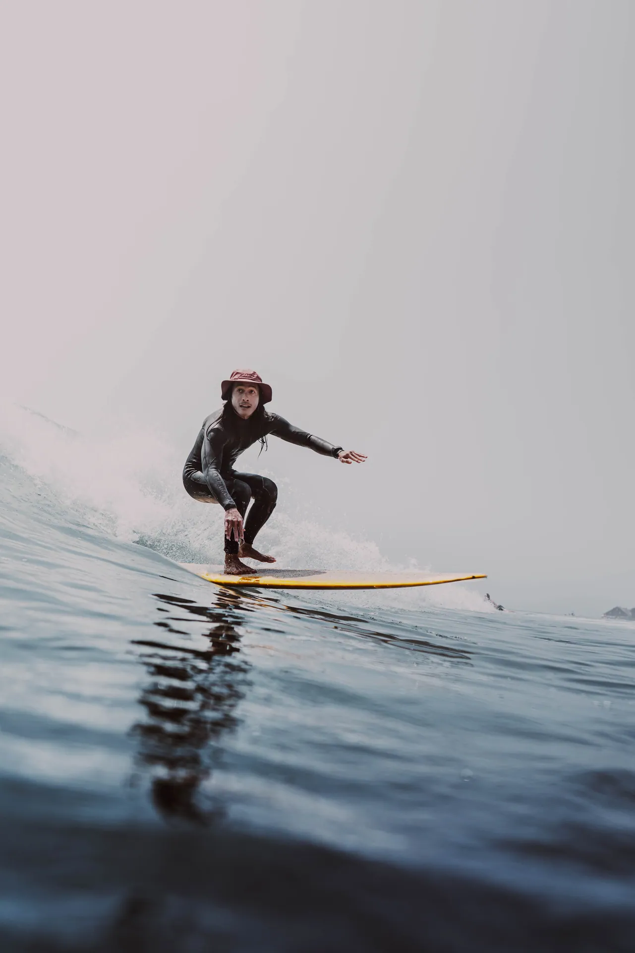 Portrait of a surfer riding a wave with a hat and wetsuit, capturing the thrill of ocean adventure.