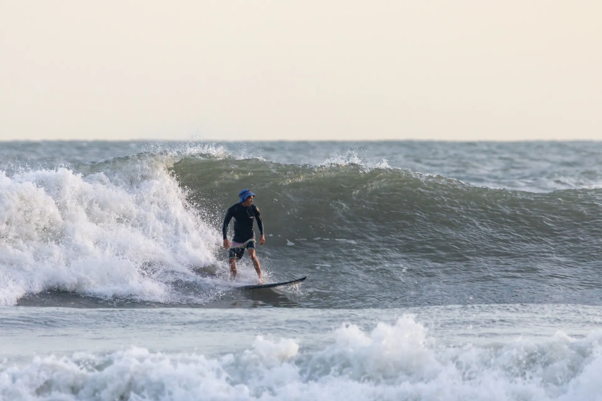 An adult male surfer expertly rides a wave in open ocean waters, showcasing surfing skills.