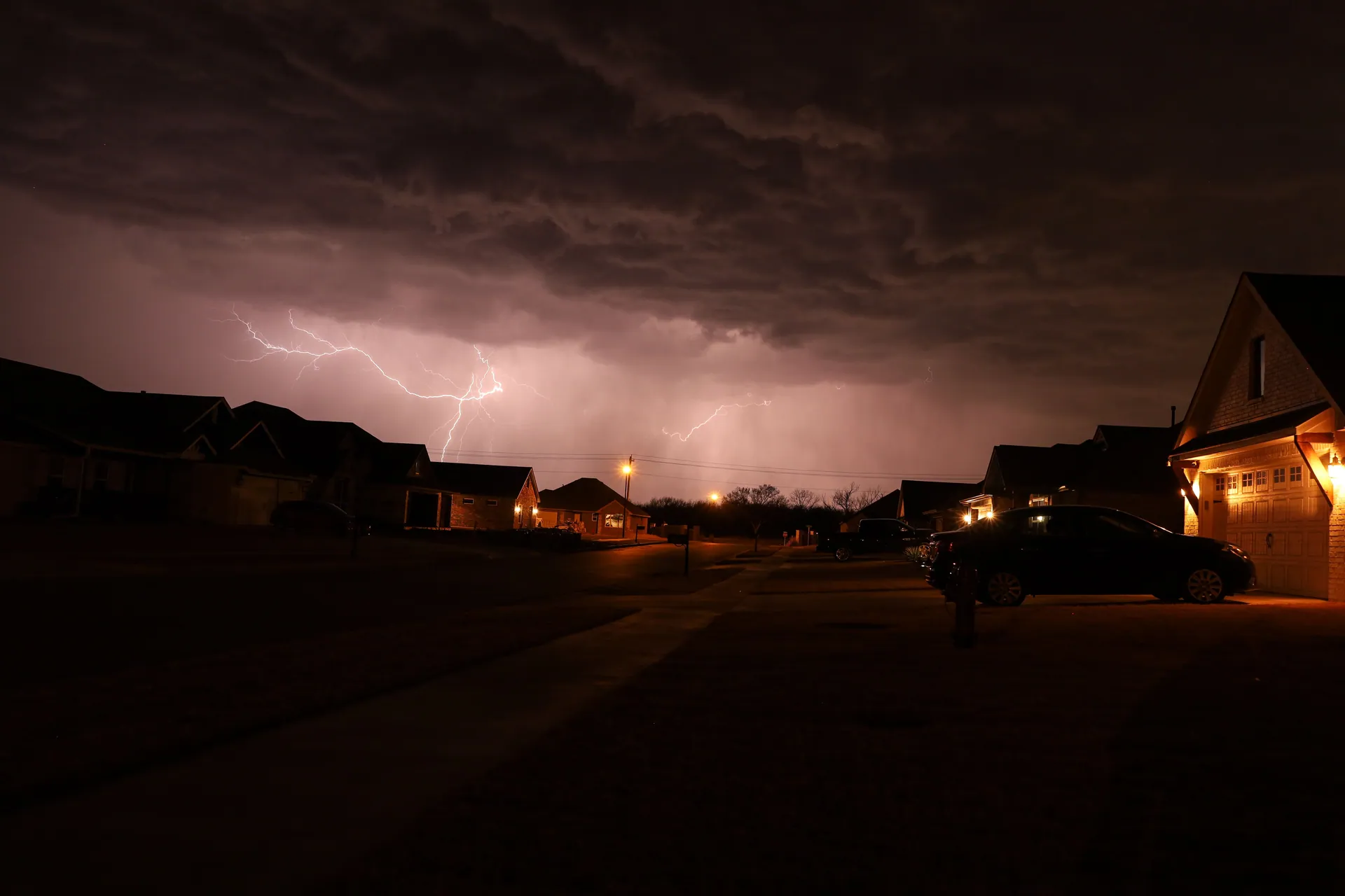 Nighttime thunderstorm with lightning illuminating a suburban neighborhood street.