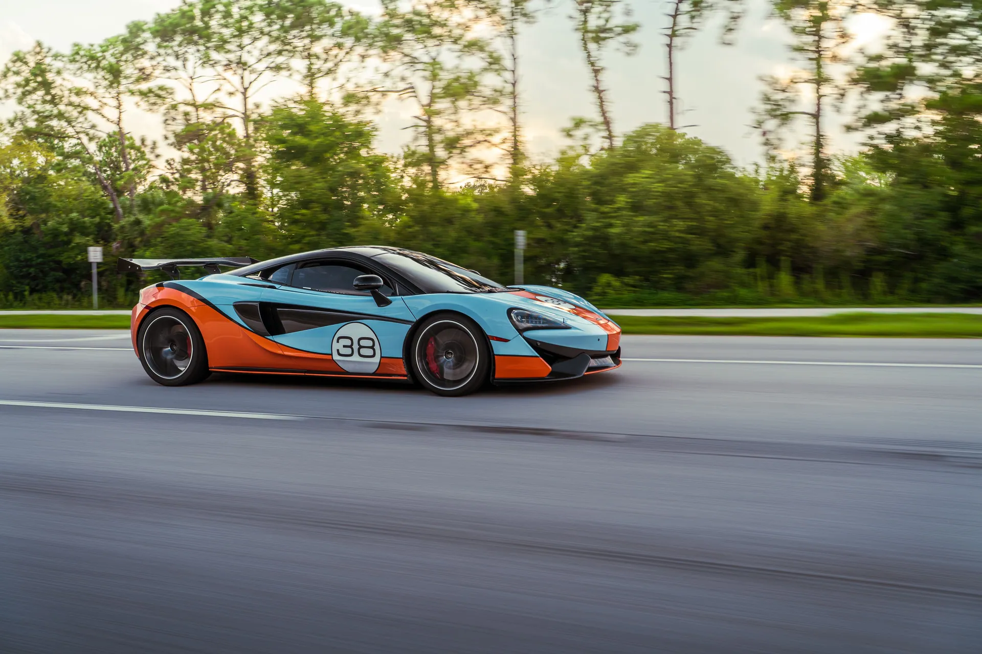Colorful sports car in motion on a highway surrounded by lush trees.