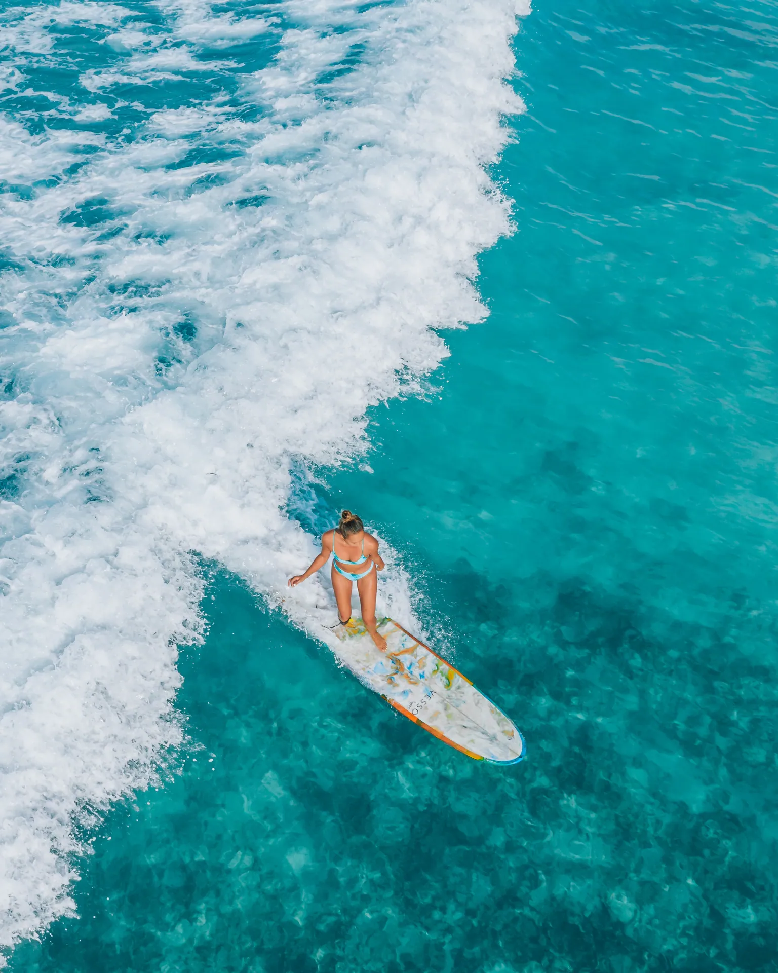 Aerial shot of a female surfer riding a turquoise ocean wave, showcasing water sports and adventure.