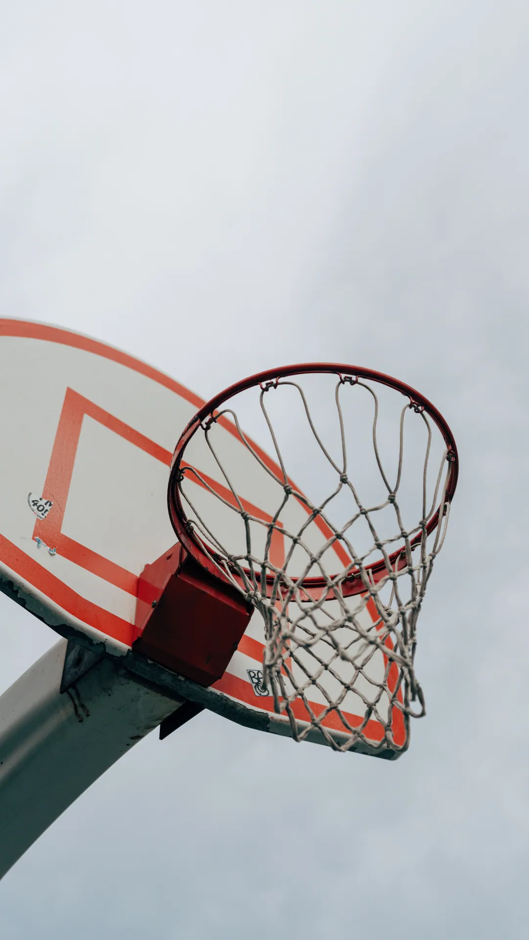 A basketball hoop and net set against a backdrop of a cloudy sky, viewed from below.