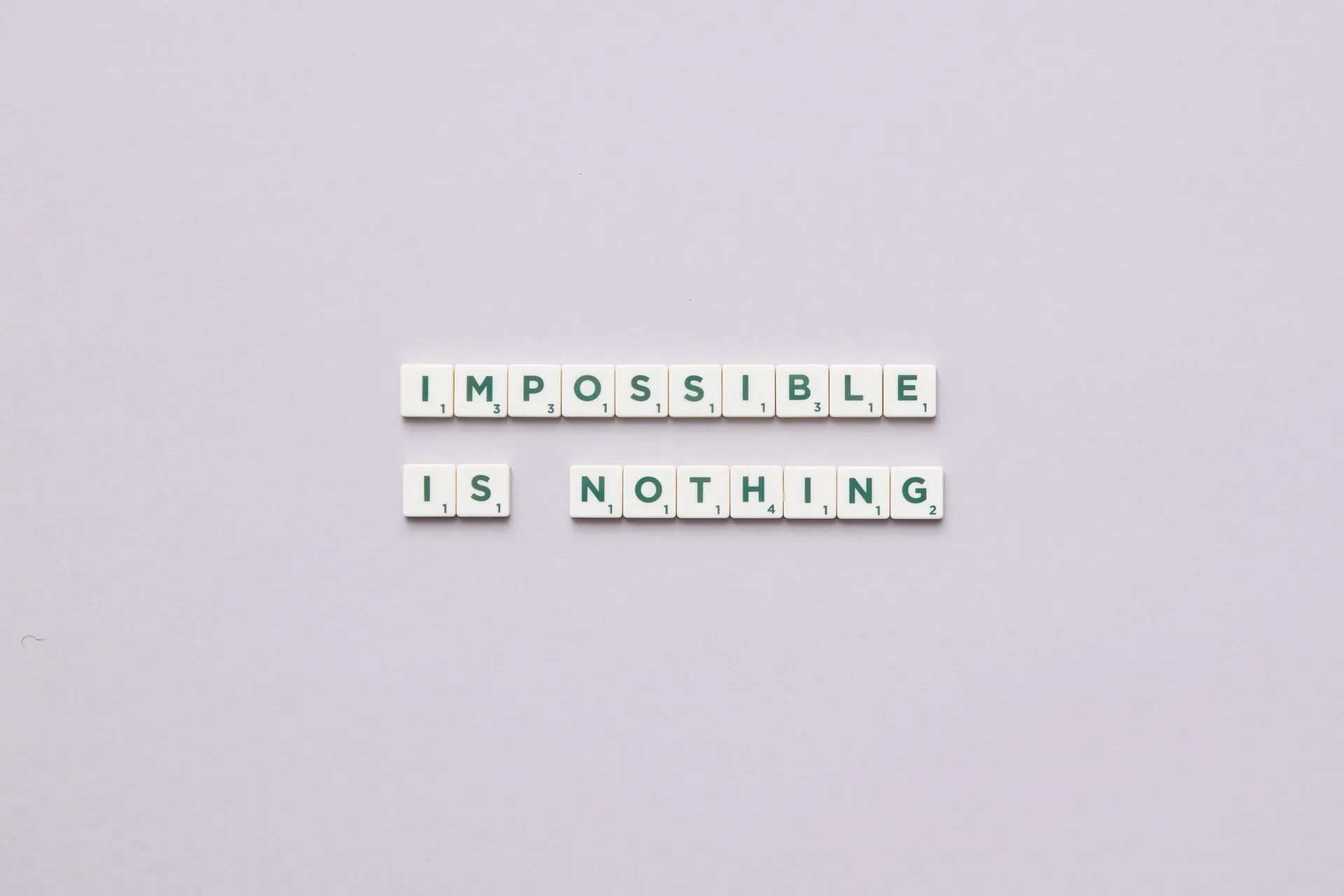 Flat lay of Scrabble tiles spelling 'Impossible is Nothing' on a neutral background.