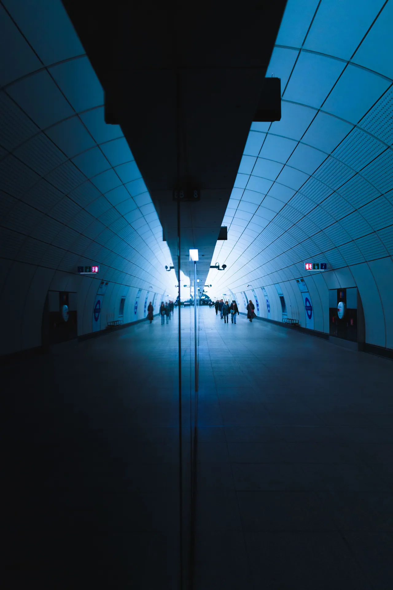 A futuristic view of London's subway with people walking through a brightly lit tunnel.