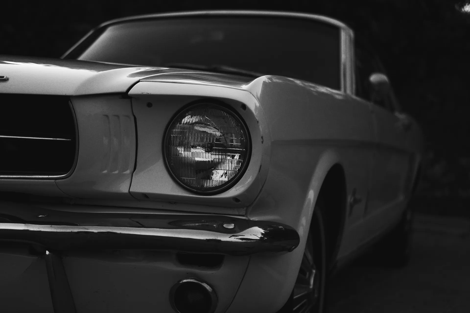 Grayscale close-up of a vintage Ford Mustang, showcasing its classic design and iconic headlights.