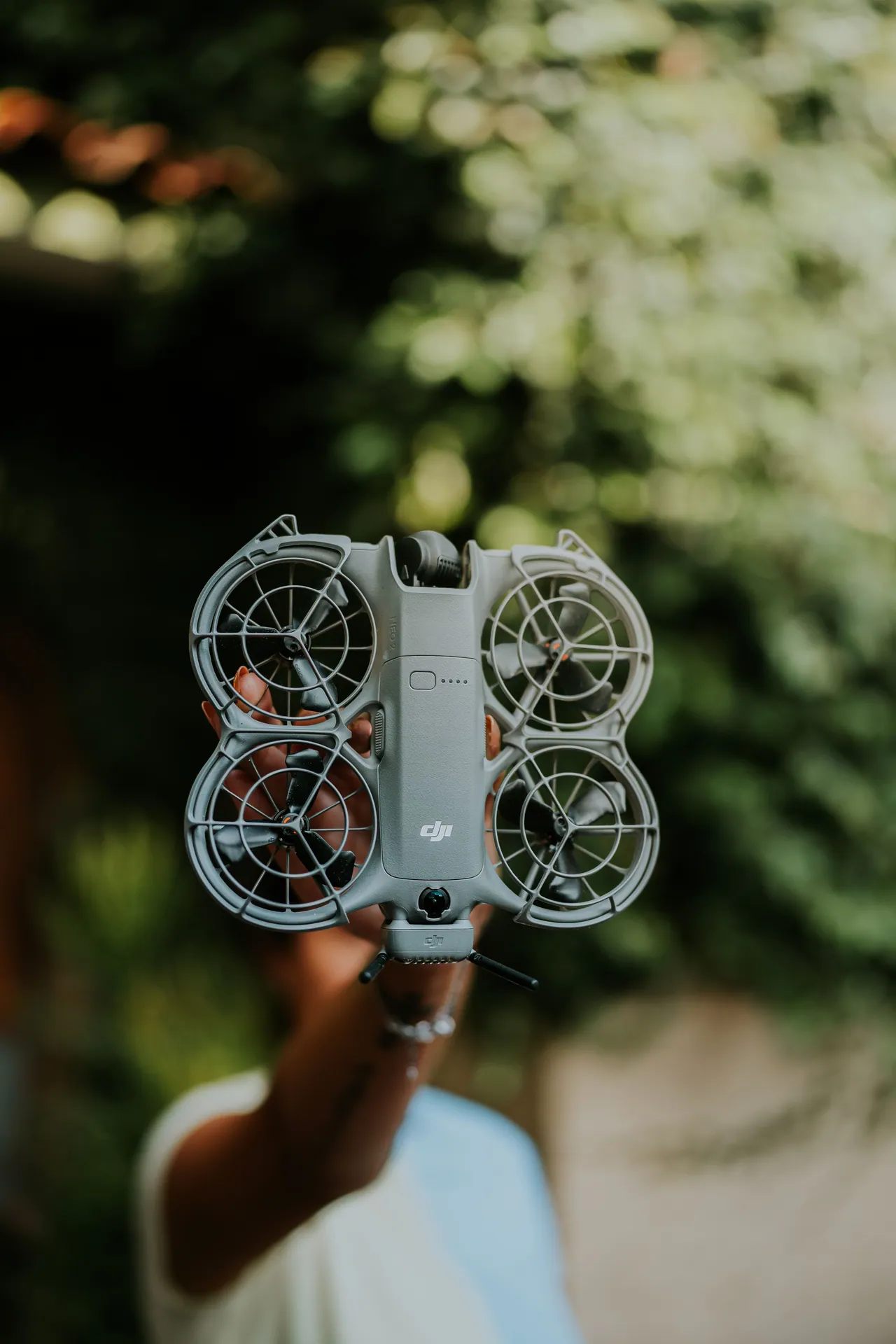 A close-up shot of a person holding a mini drone with propeller guards in a natural outdoor setting.