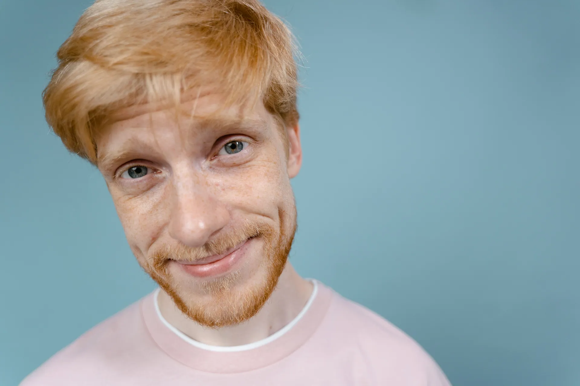 Cheerful bearded man with blonde hair smiling against a light blue background.