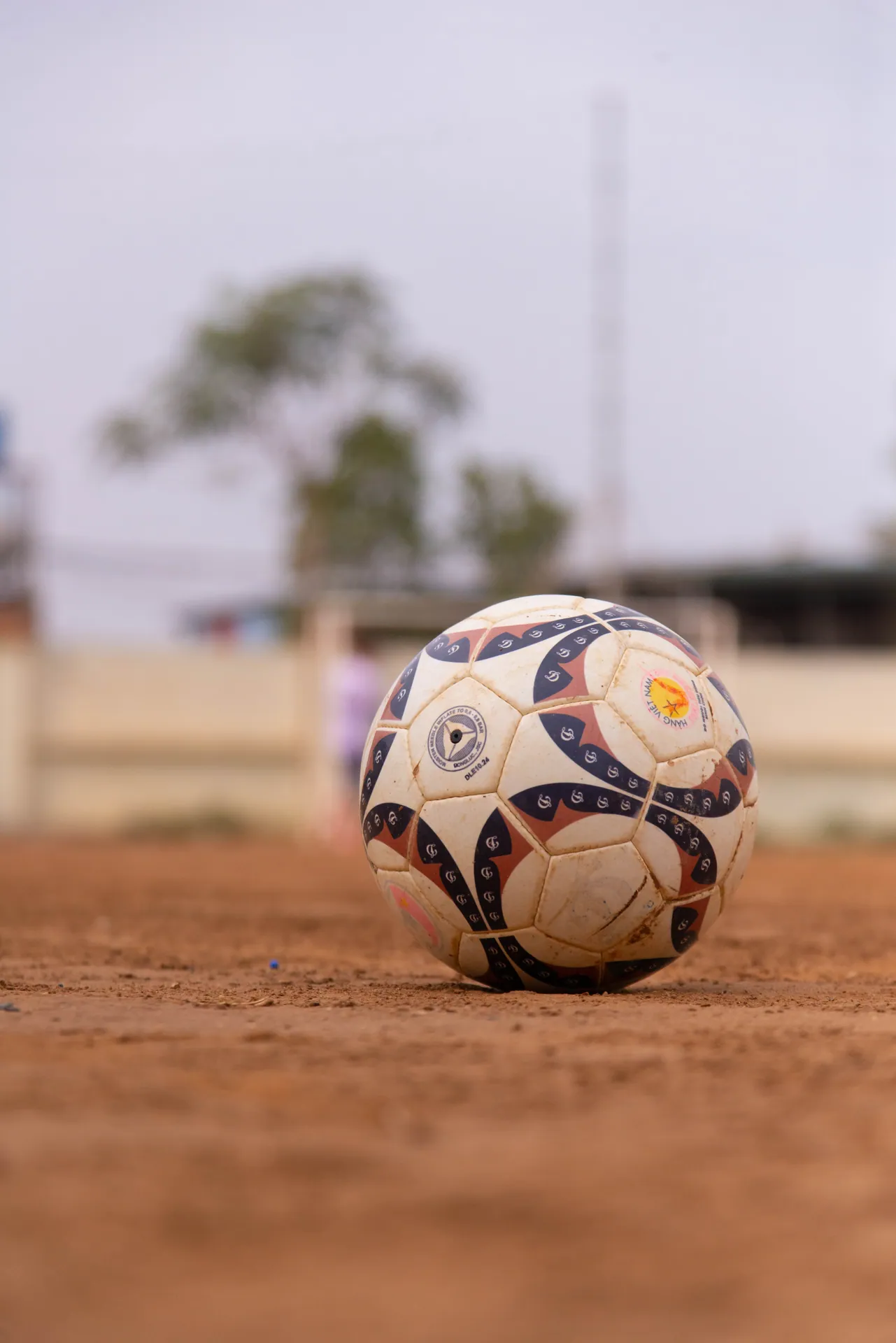 Close-up of a soccer ball on a dirt field outdoors in the daytime.