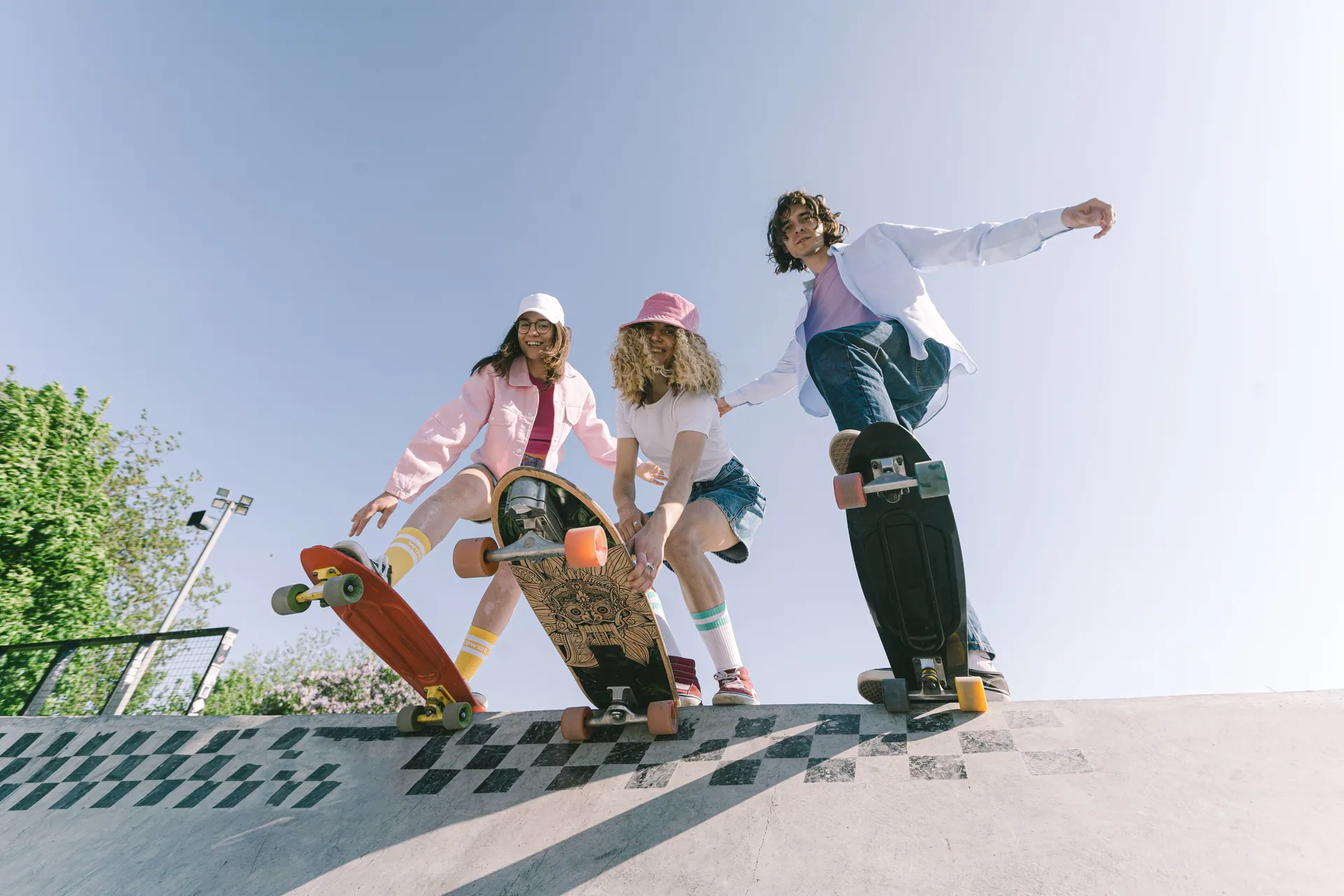 Three skateboarders in vibrant outfits having fun at a skate park ramp on a sunny day.