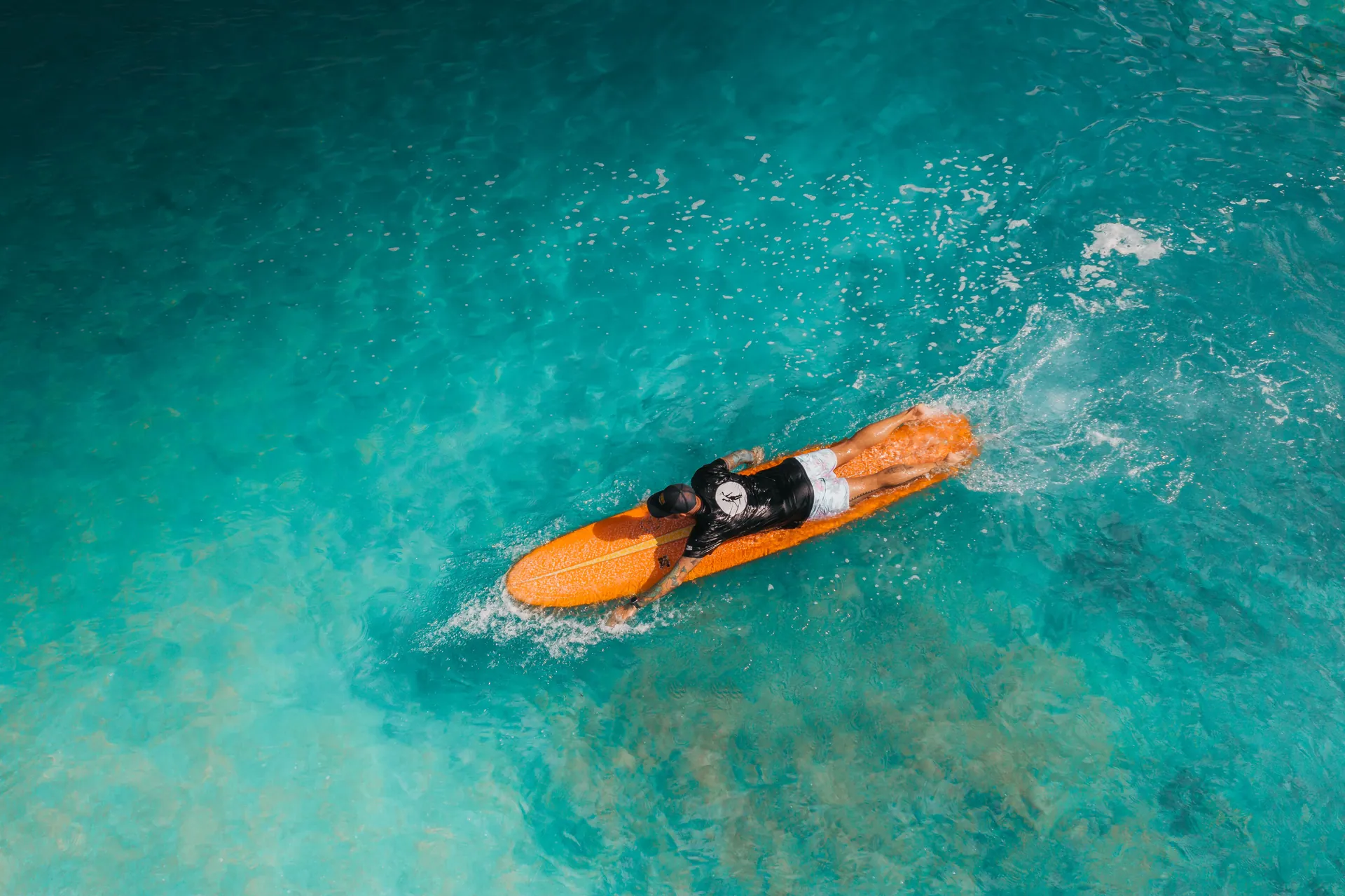 Top-down shot of a surfer paddling on a vibrant turquoise sea, showcasing summer adventure.