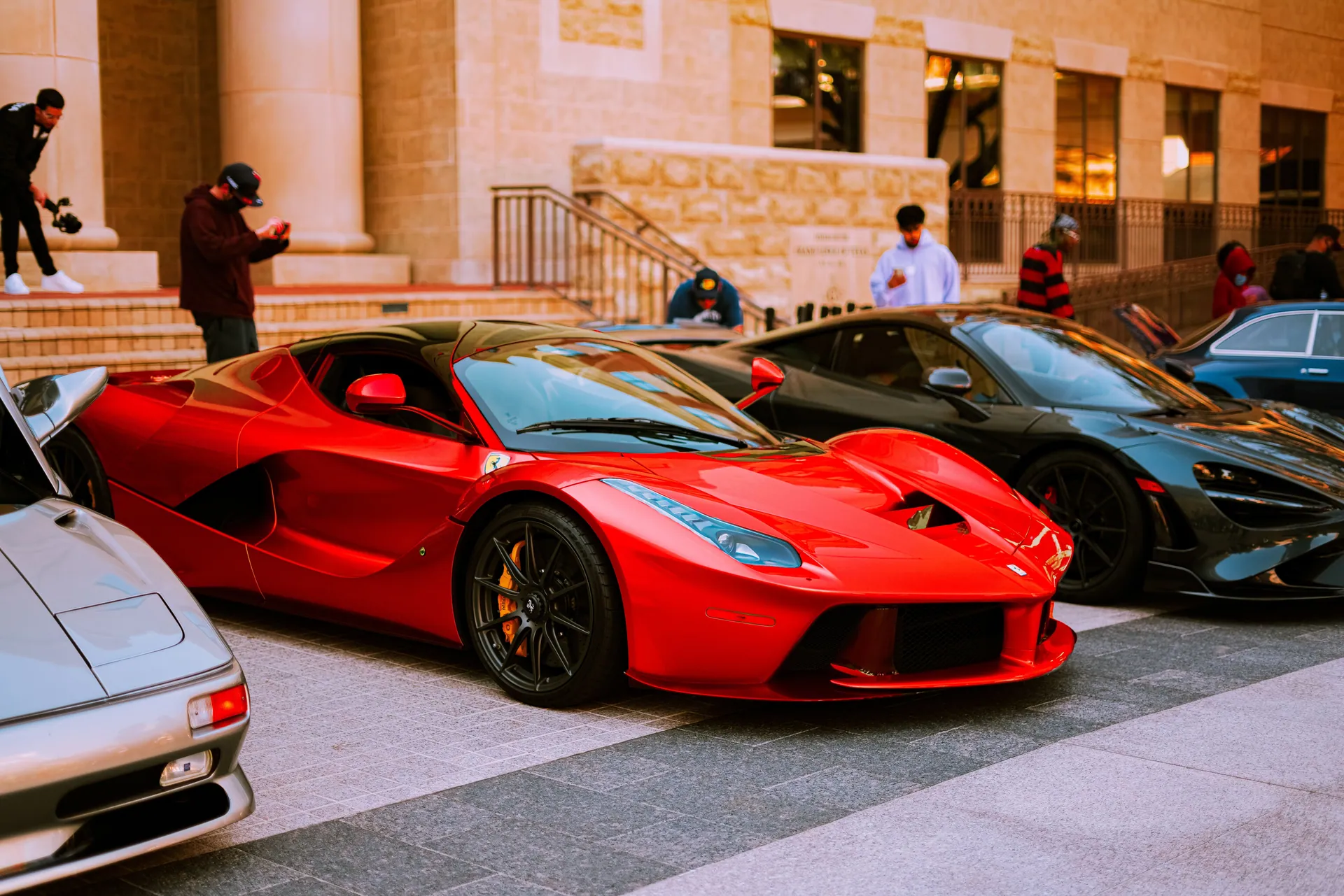 A lineup of luxury sports cars parked on an urban street during the day.