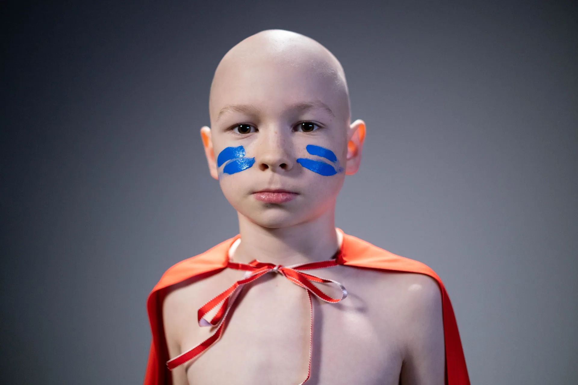Inspirational studio portrait of a young child with face paint, embracing inner strength in a superhero cape.