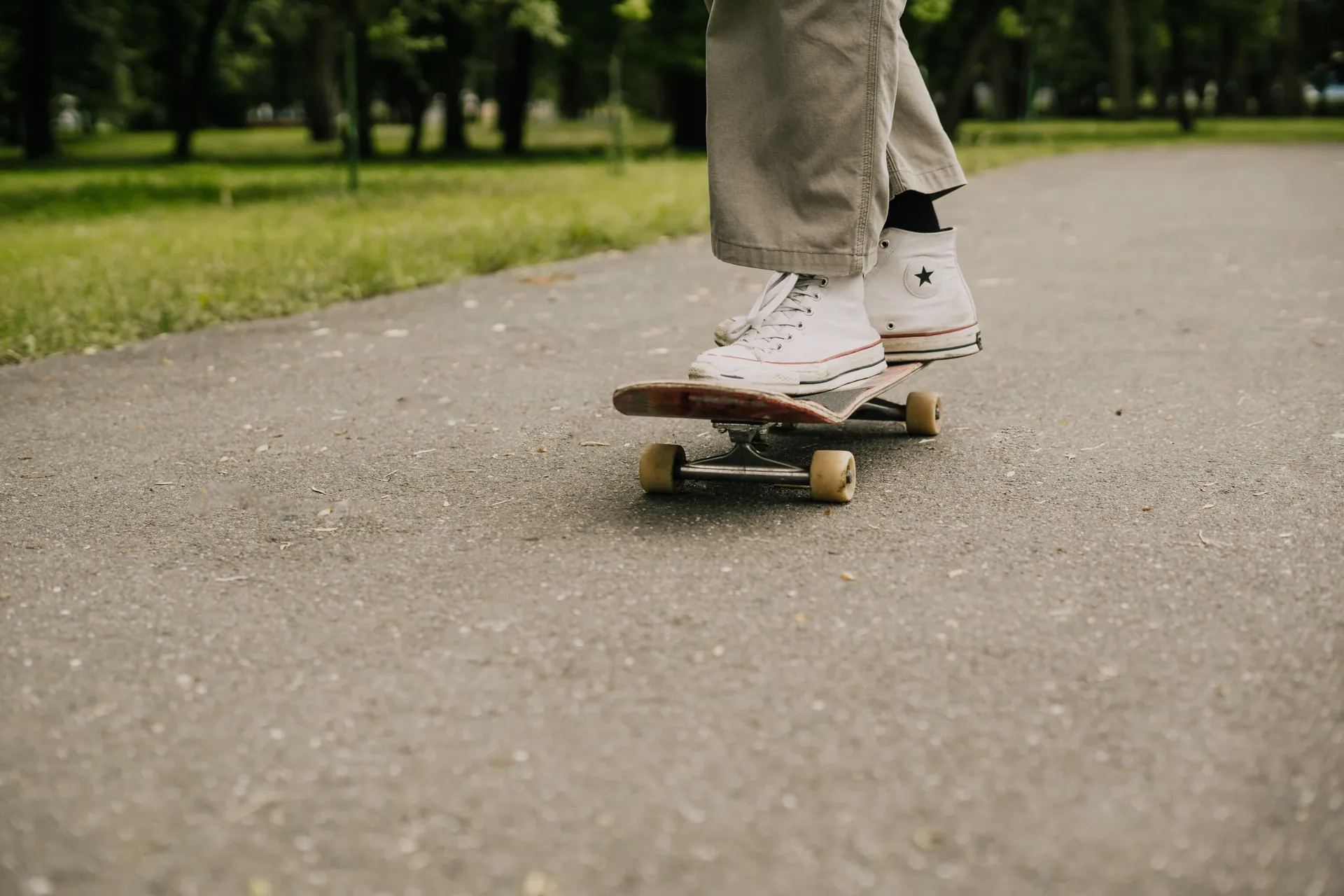 Close-up of a skateboarder in white sneakers riding in a park on a sunny day.