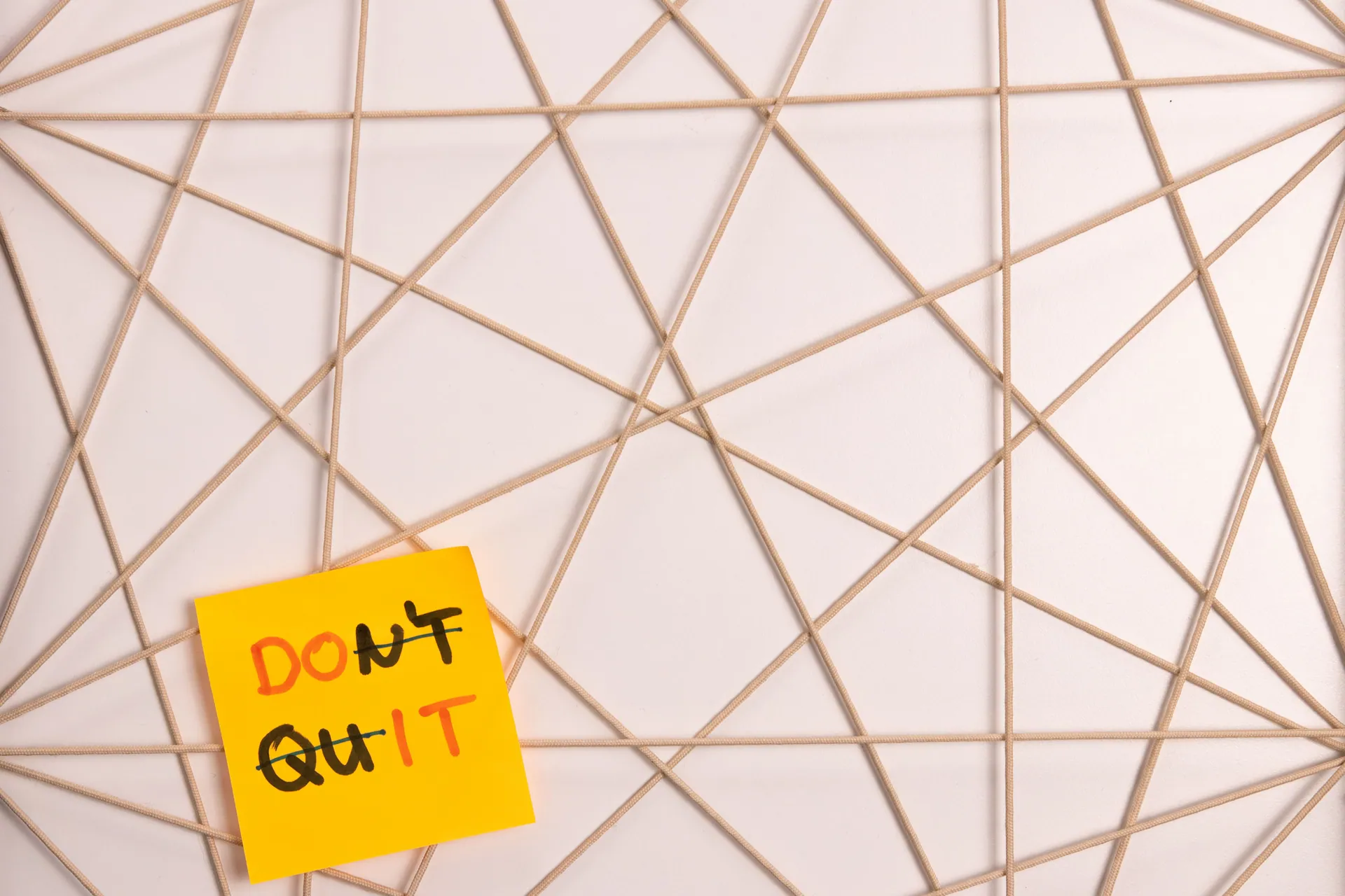 Bright yellow sticky note with motivational message on an abstract geometric design background.