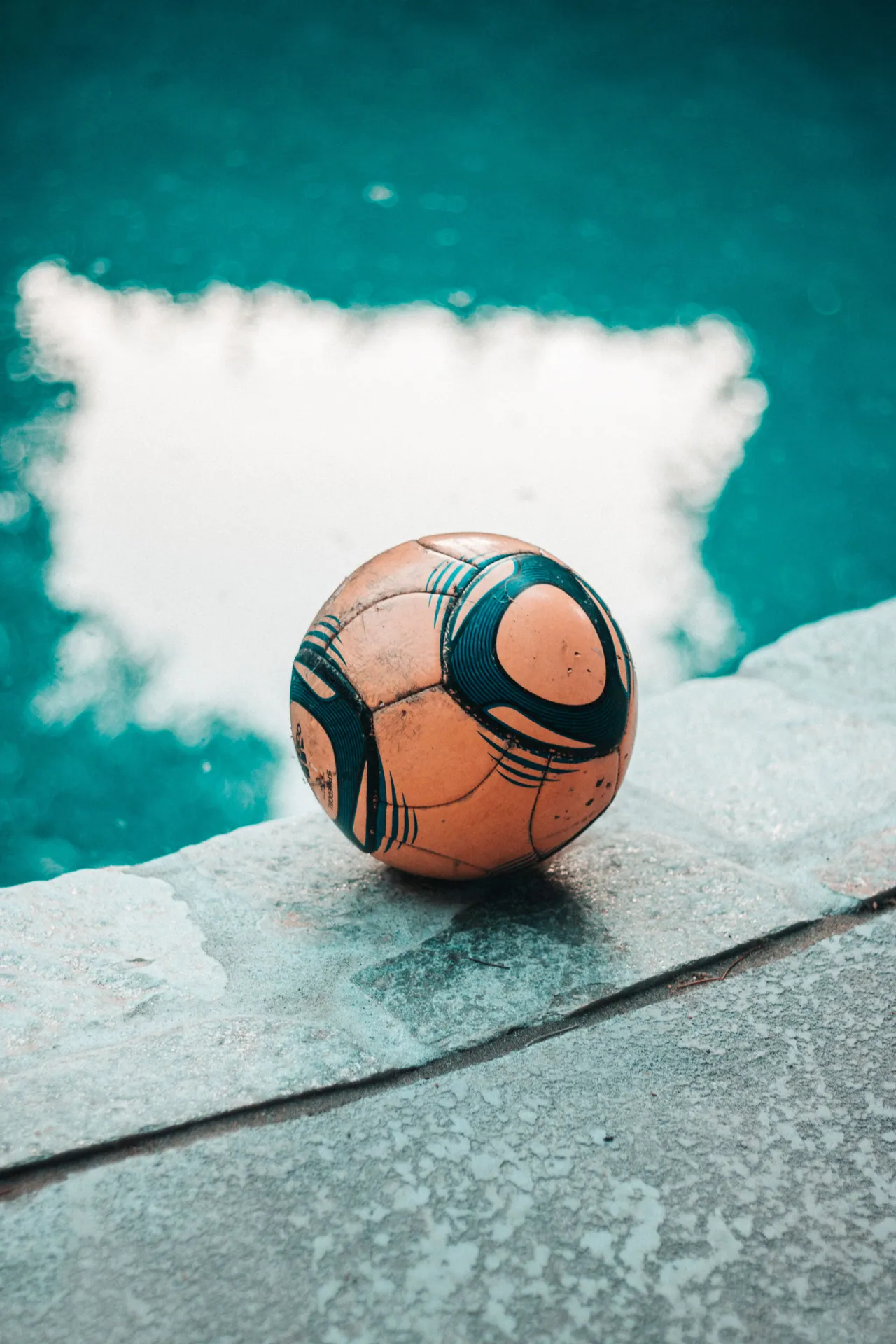 A soccer ball rests on the edge of a swimming pool under clear skies, evoking relaxation.