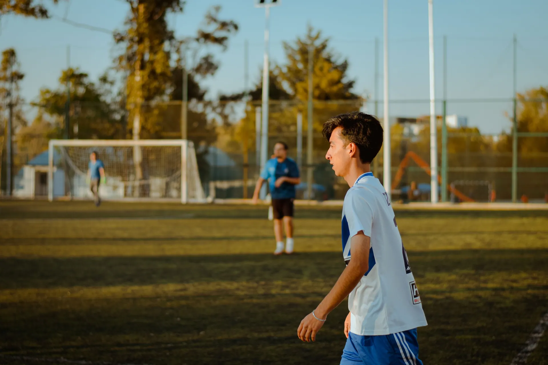 A teenager plays soccer outdoors on a sunny day, enjoying friendly competition.