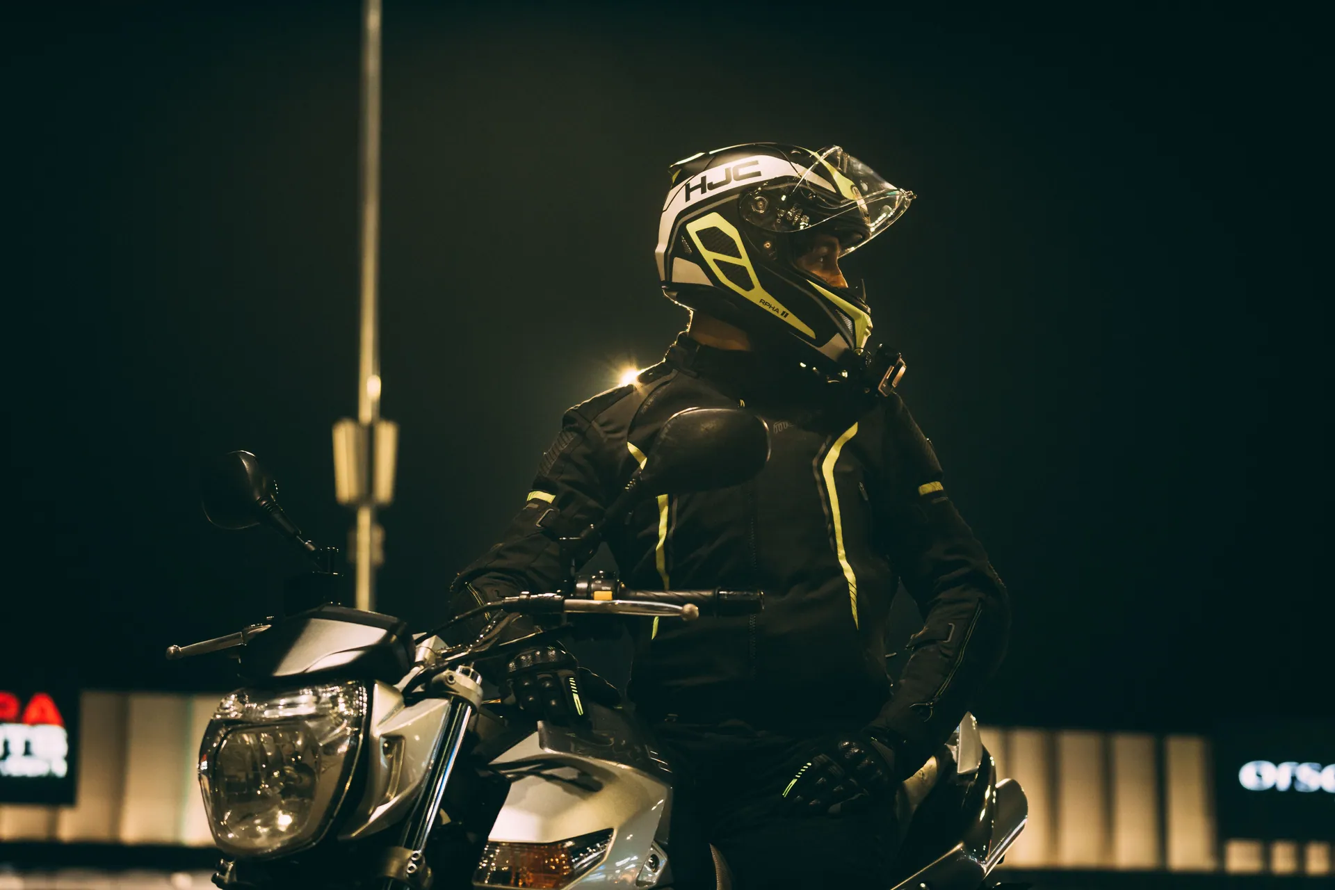 A motorcyclist in black gear and helmet looks back while riding at night in Serbia.